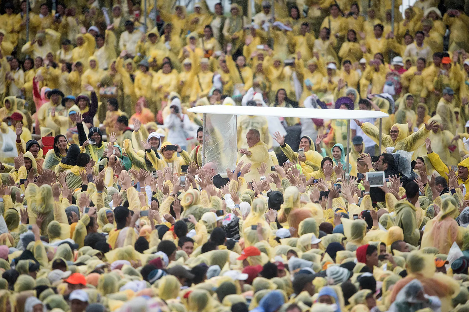 Pope Francis in a plastic poncho is surrounded by people