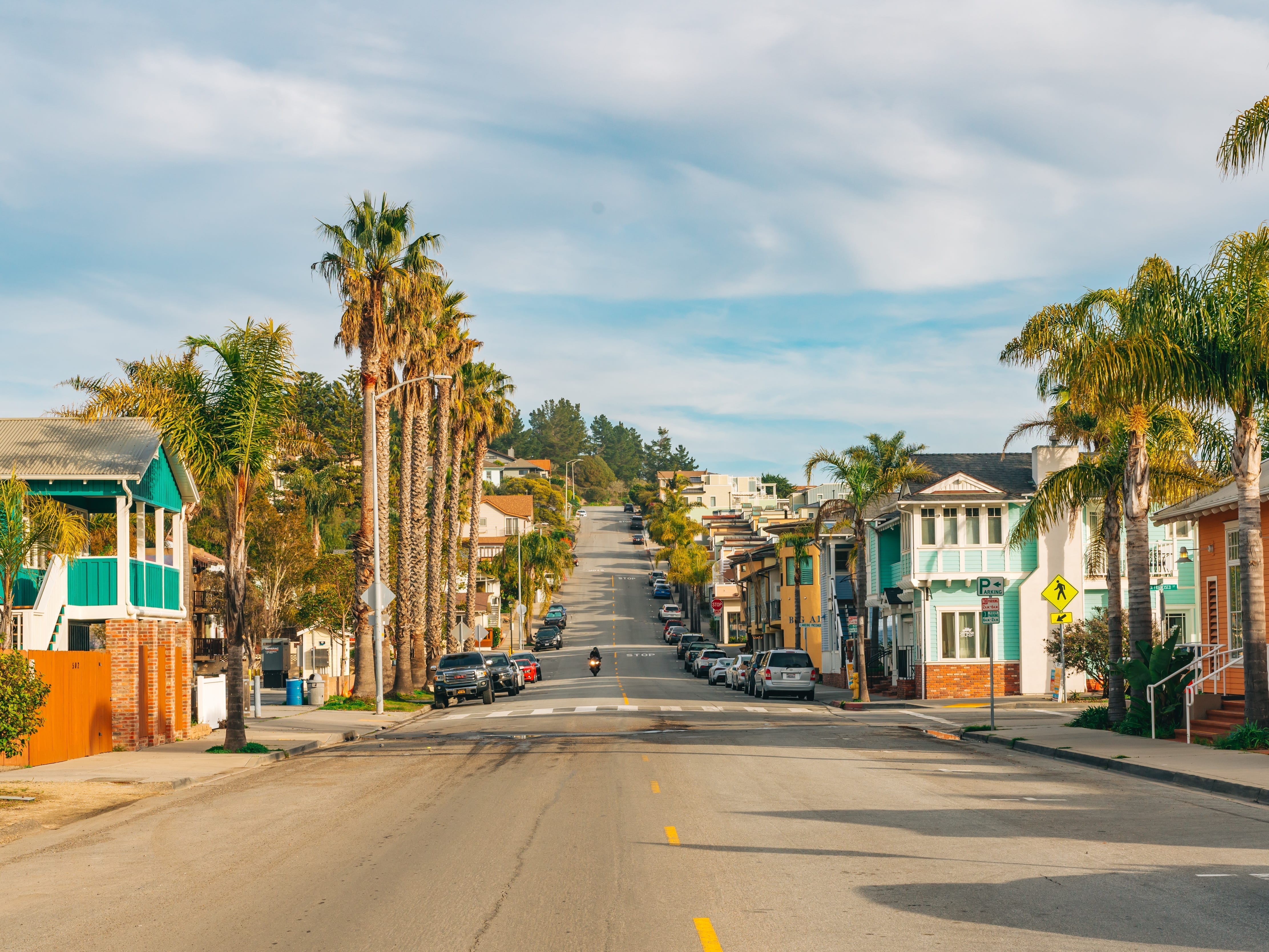 A street in Avila Beach, California, with houses and palm trees on either side of the road.