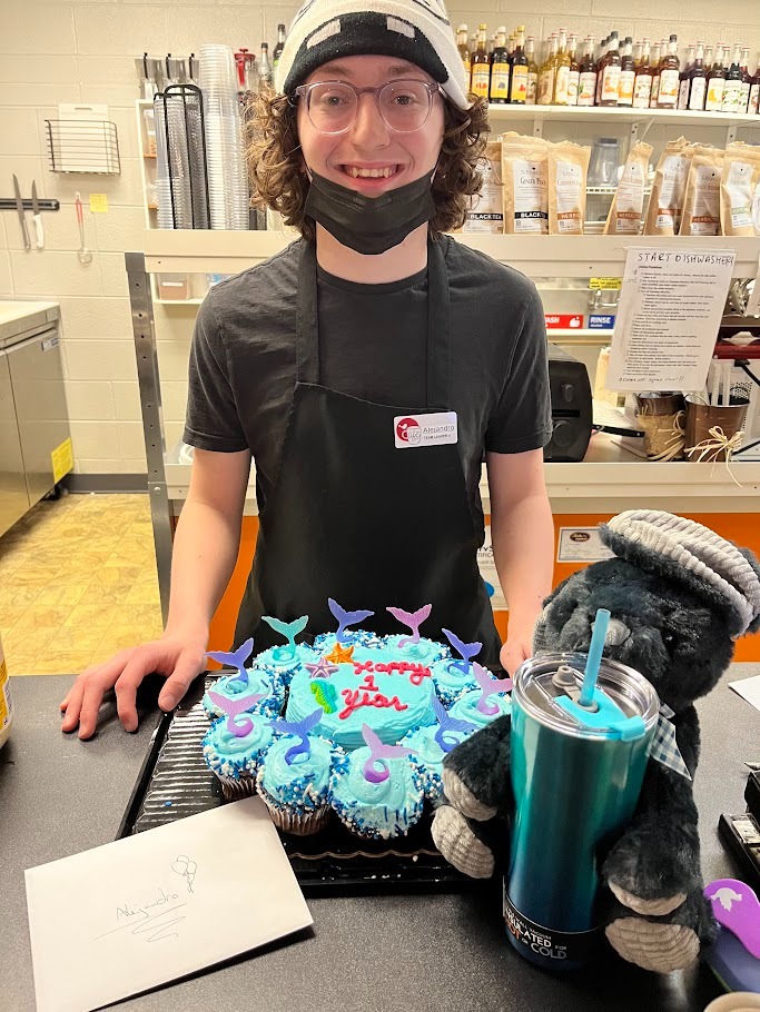 Alejandro poses with a plate of cupcakes celebrating an anniversary at his work.
