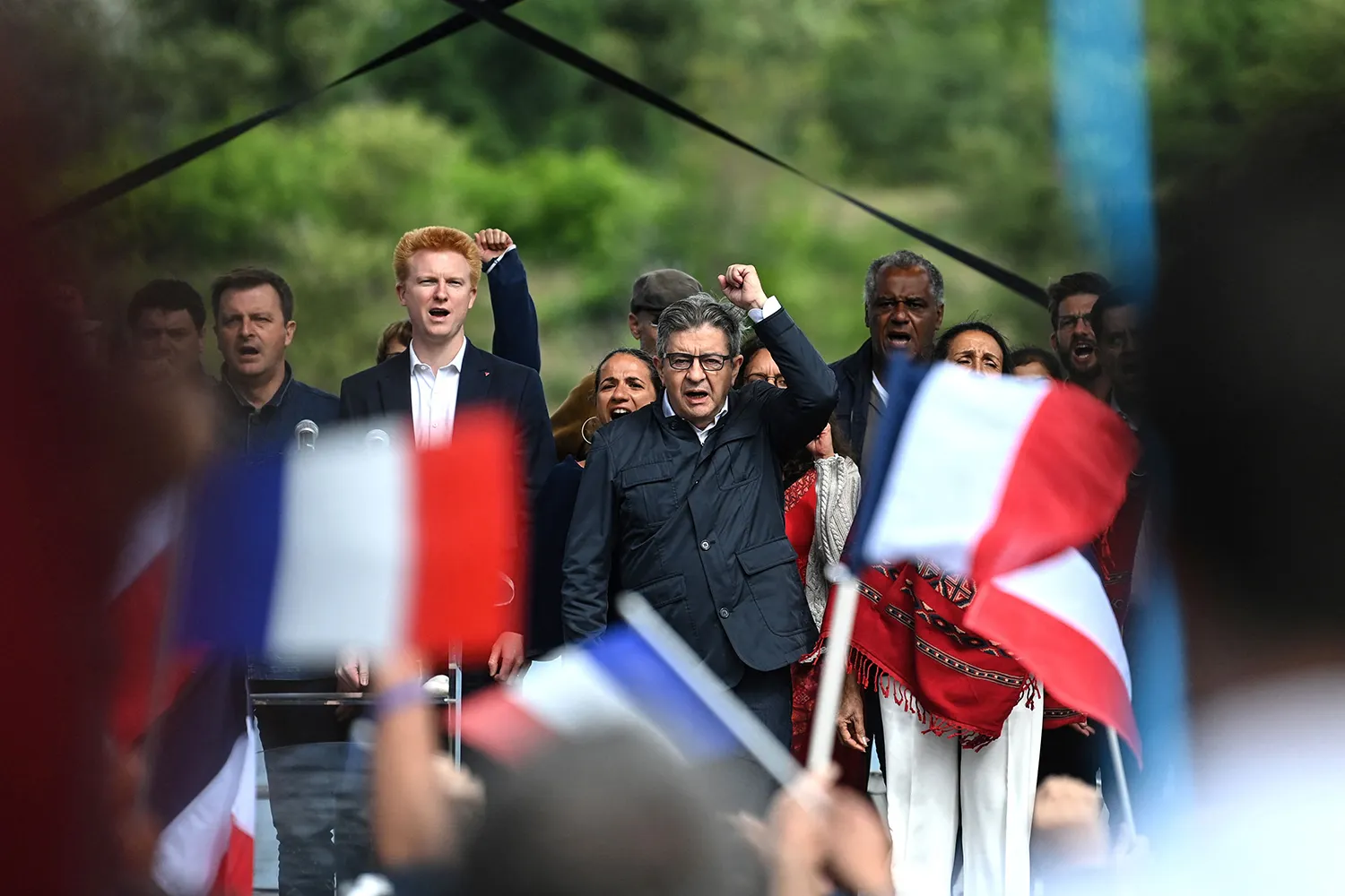Mélenchon and Adrien Quatennens on stage with French flags in the foreground.
