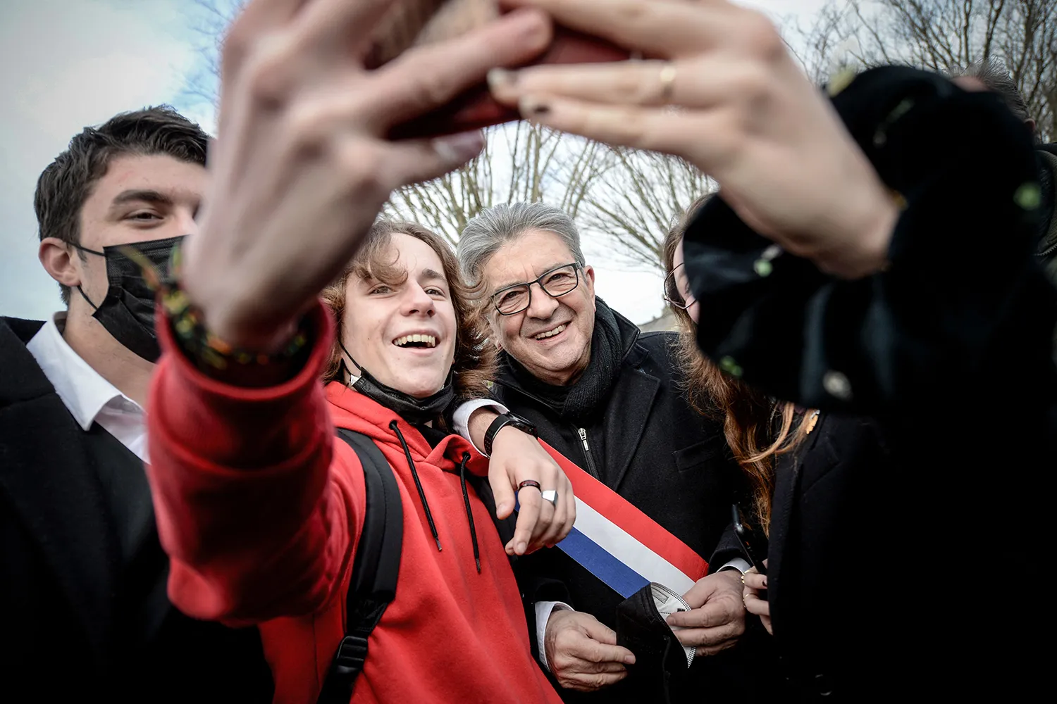 Mélenchon poses for a selfie with supporters outside.