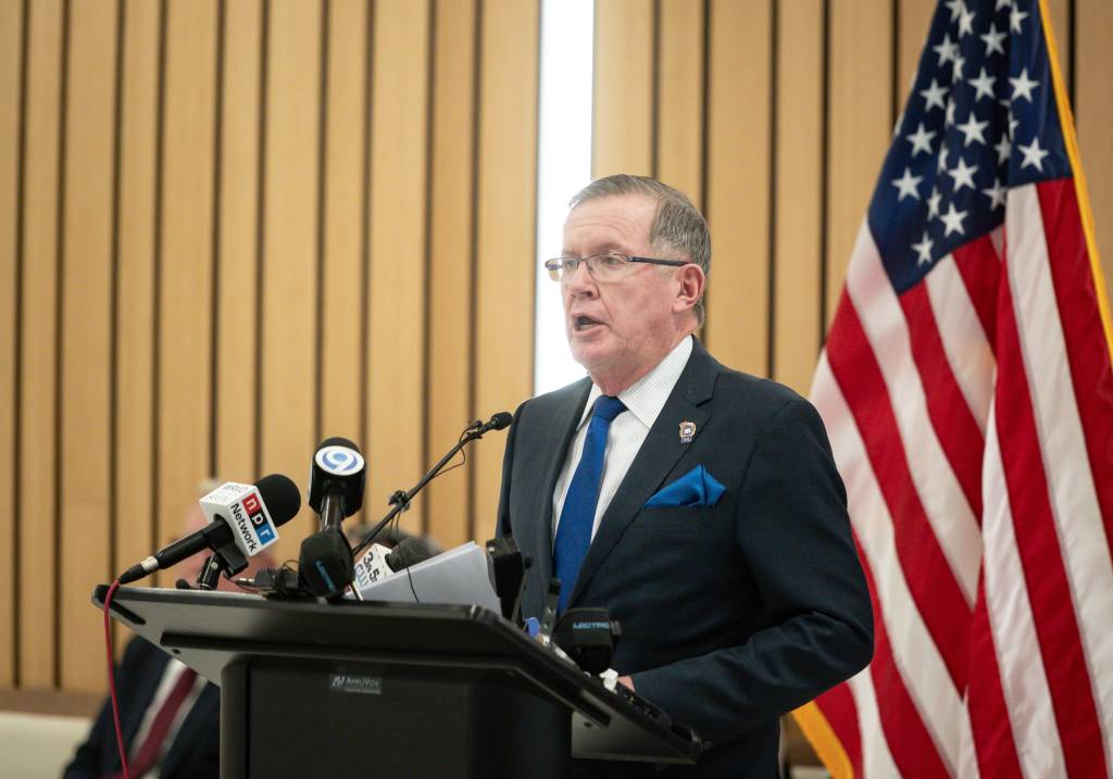 Onondaga County District Attorney William J. Fitzpatrick speaking at a podium during a press conference about indictments against former Marcy correction officers, with microphones and a flag in the background