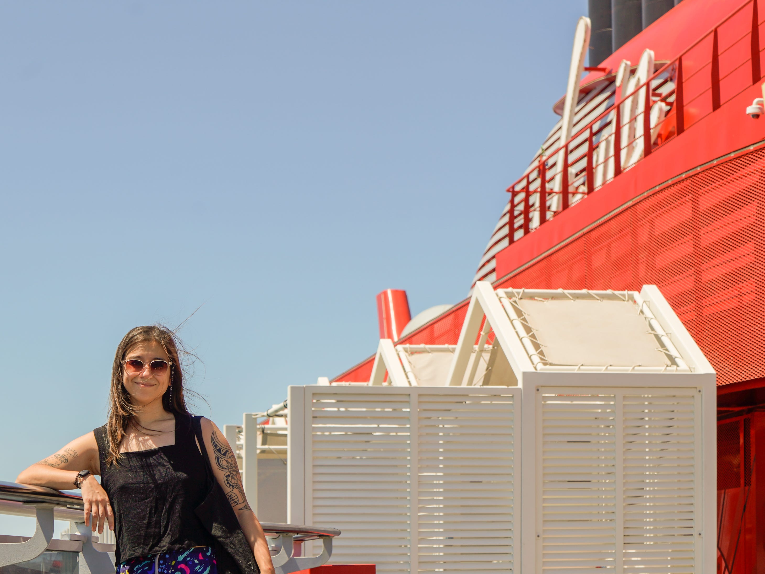 The author leans against the side of a cruise ship with blue skies behind her.