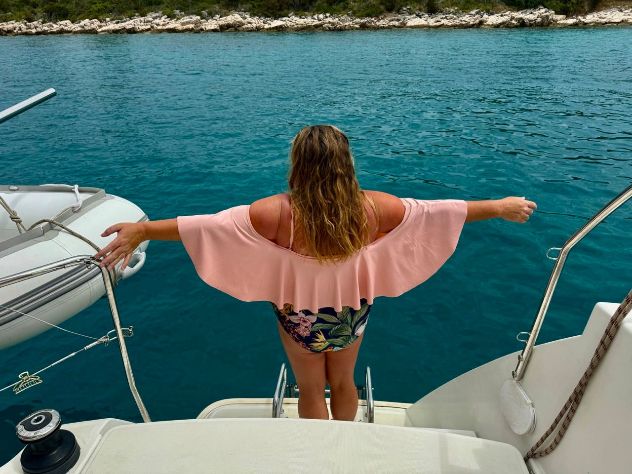 Author Tammy Barr with arms spread on boat in front of turquoise waters 