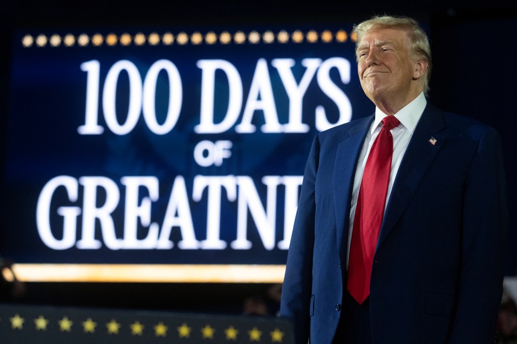 President Donald Trump stands in front of a sign marking his 100th day in office during a rally at Macomb County Community College in Warren, Michigan on April 29, 2025. 