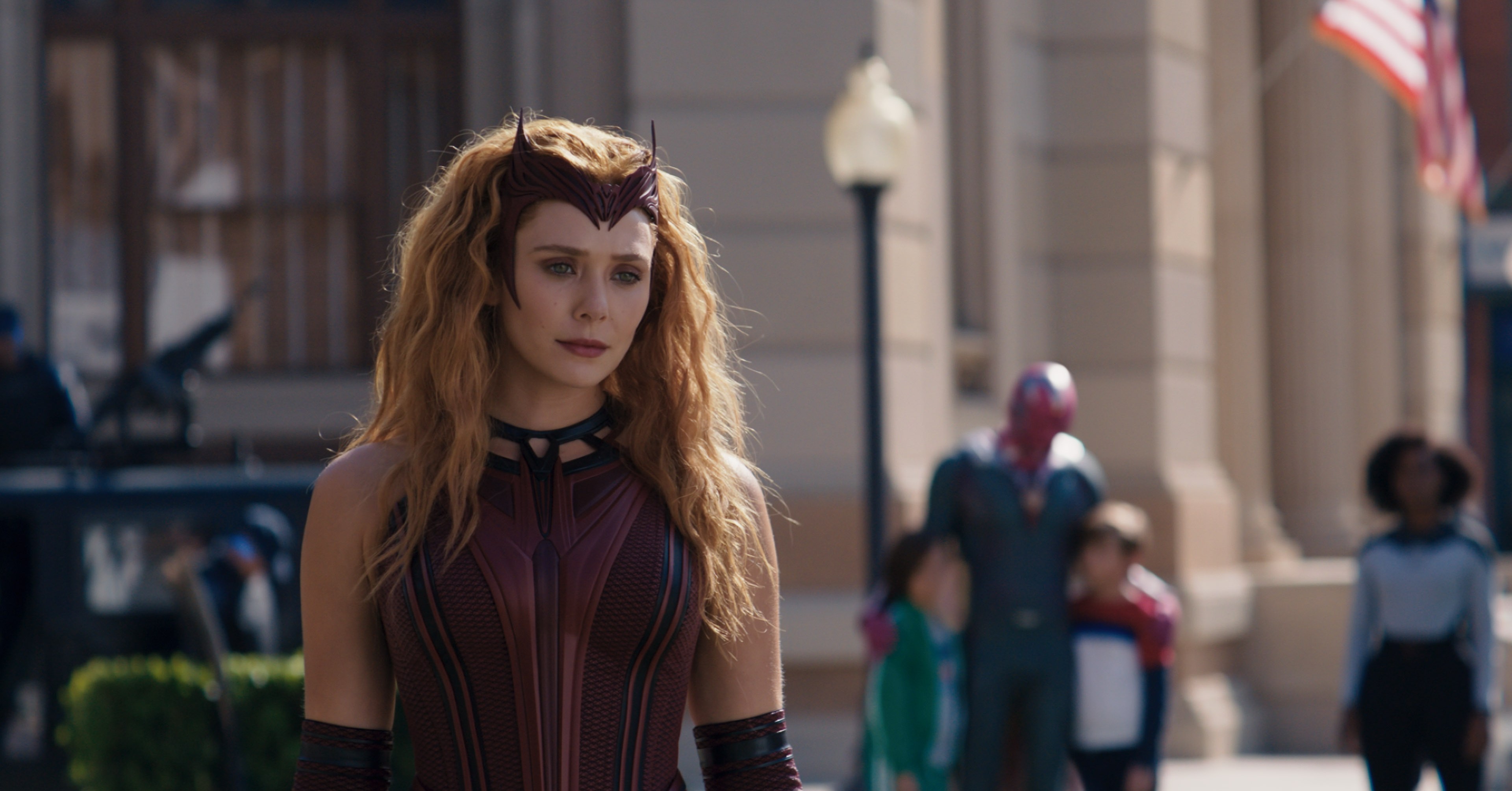 Wanda in her new Scarlet Witch costume stands in front of Vision and their two kids