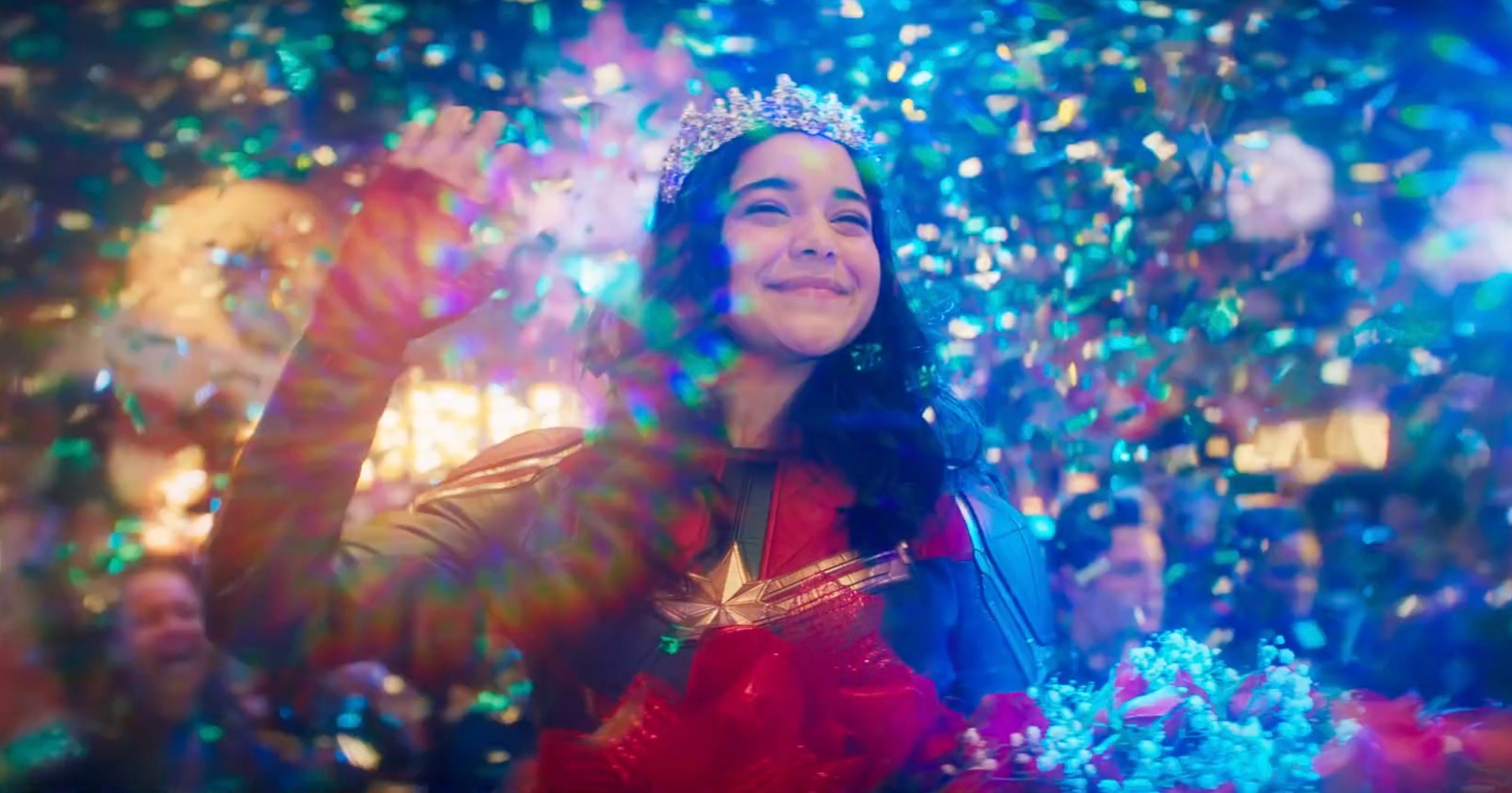 Kamala Khan waves in her Ms. Marvel costume as bright lights and confetti sprays around her