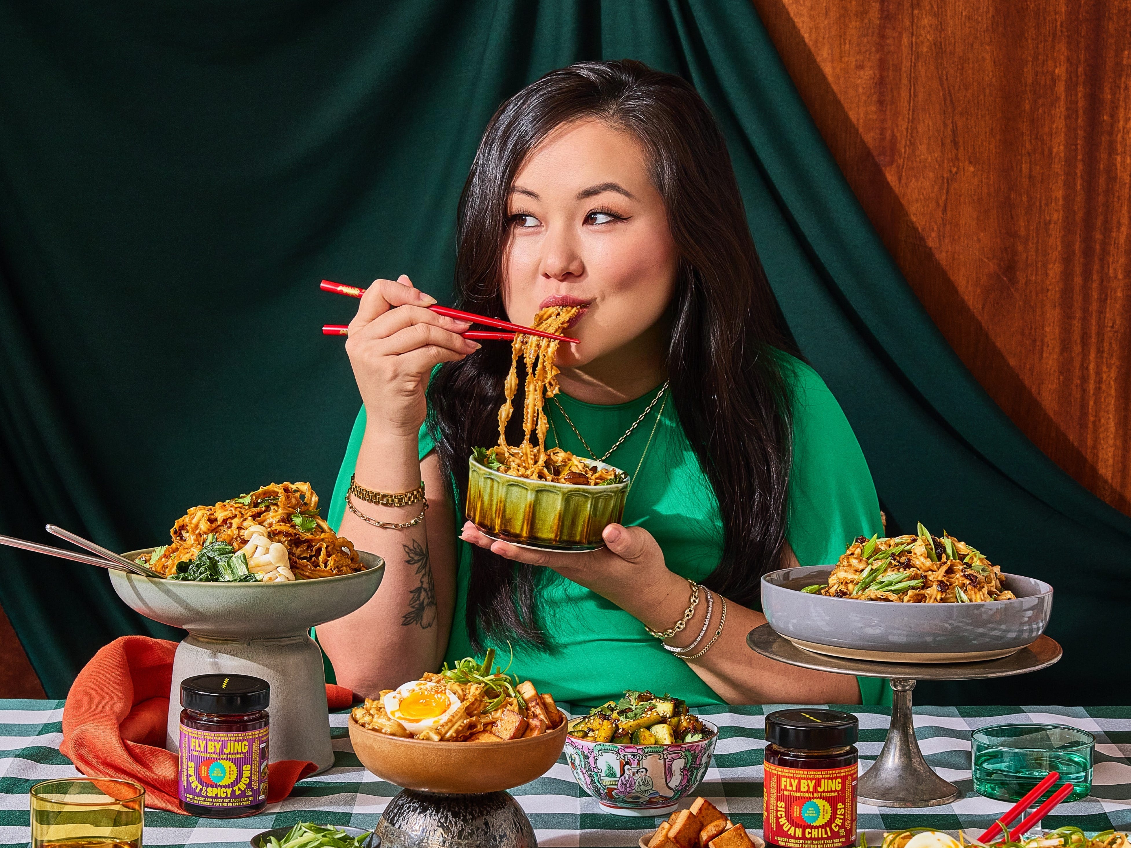 Jing Gao, founder and CEO of chili crisp company Fly By Jing, sits at a table with various food dishes