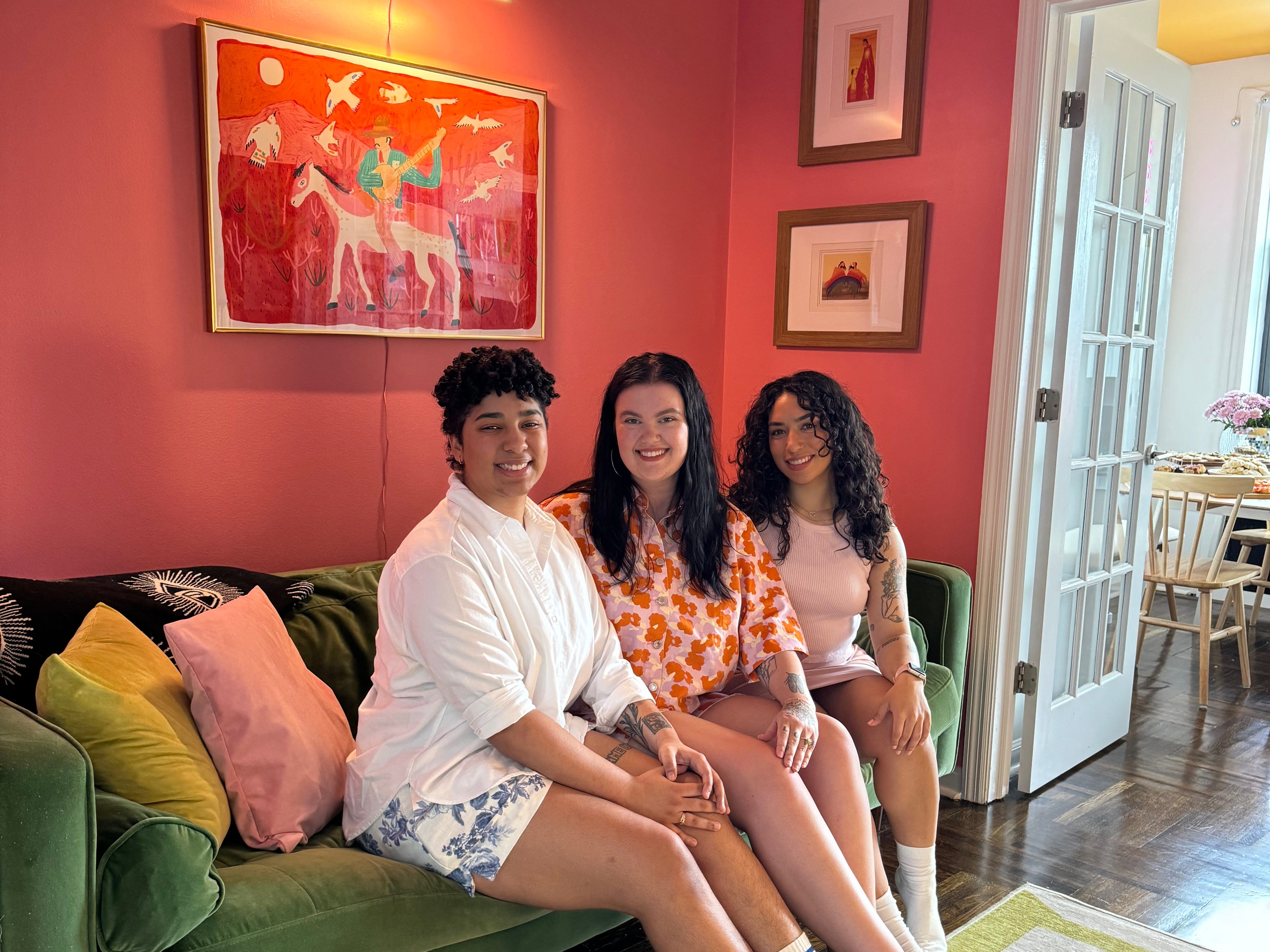 The author sitting on a green velvet couch with her wife and sister-in-law in a room with pink walls and a colorful rug.