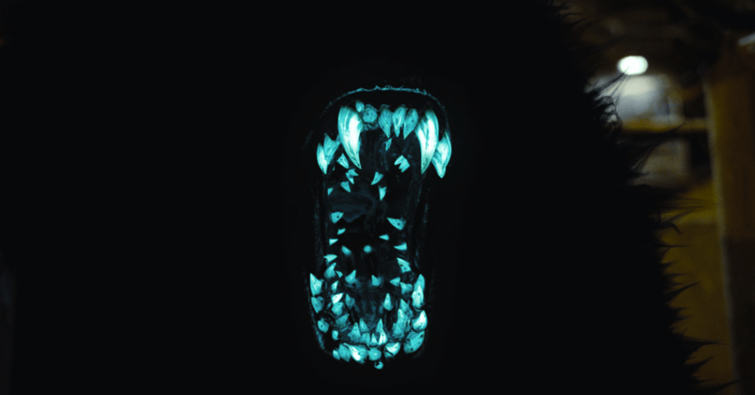 A mouth filled with blue glowing teeth set in the jaw of a jet black furry monster.