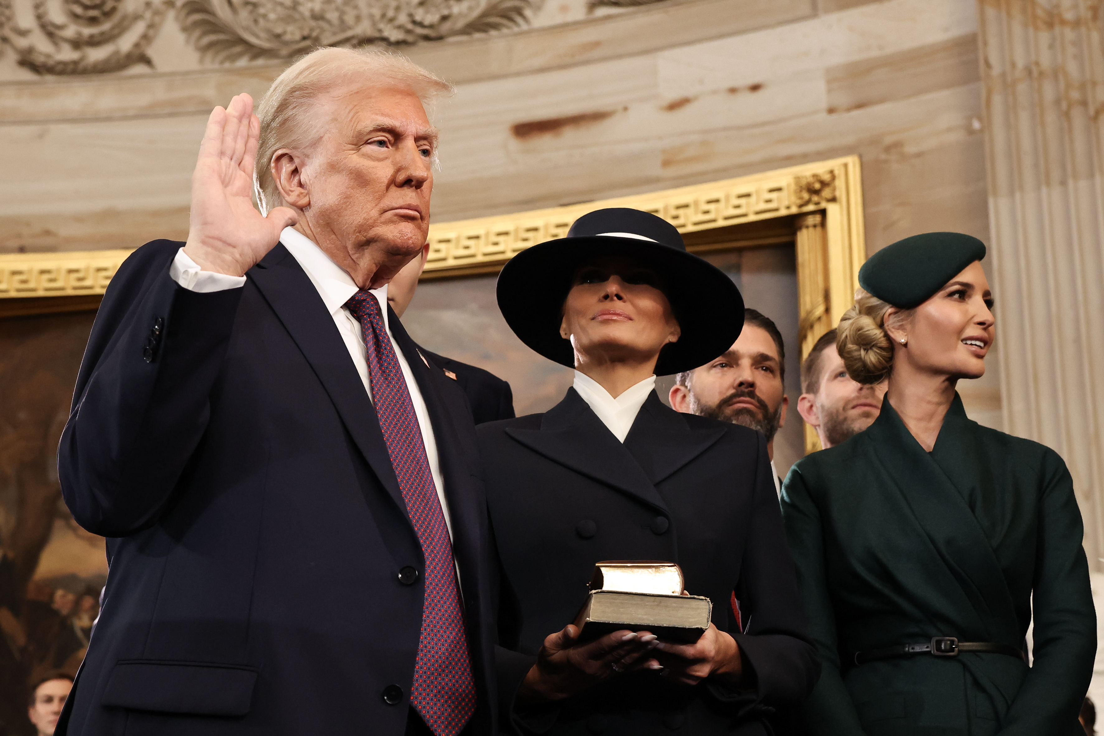 Melania Trump holds a Bible as Donald Trump raises his arm. 