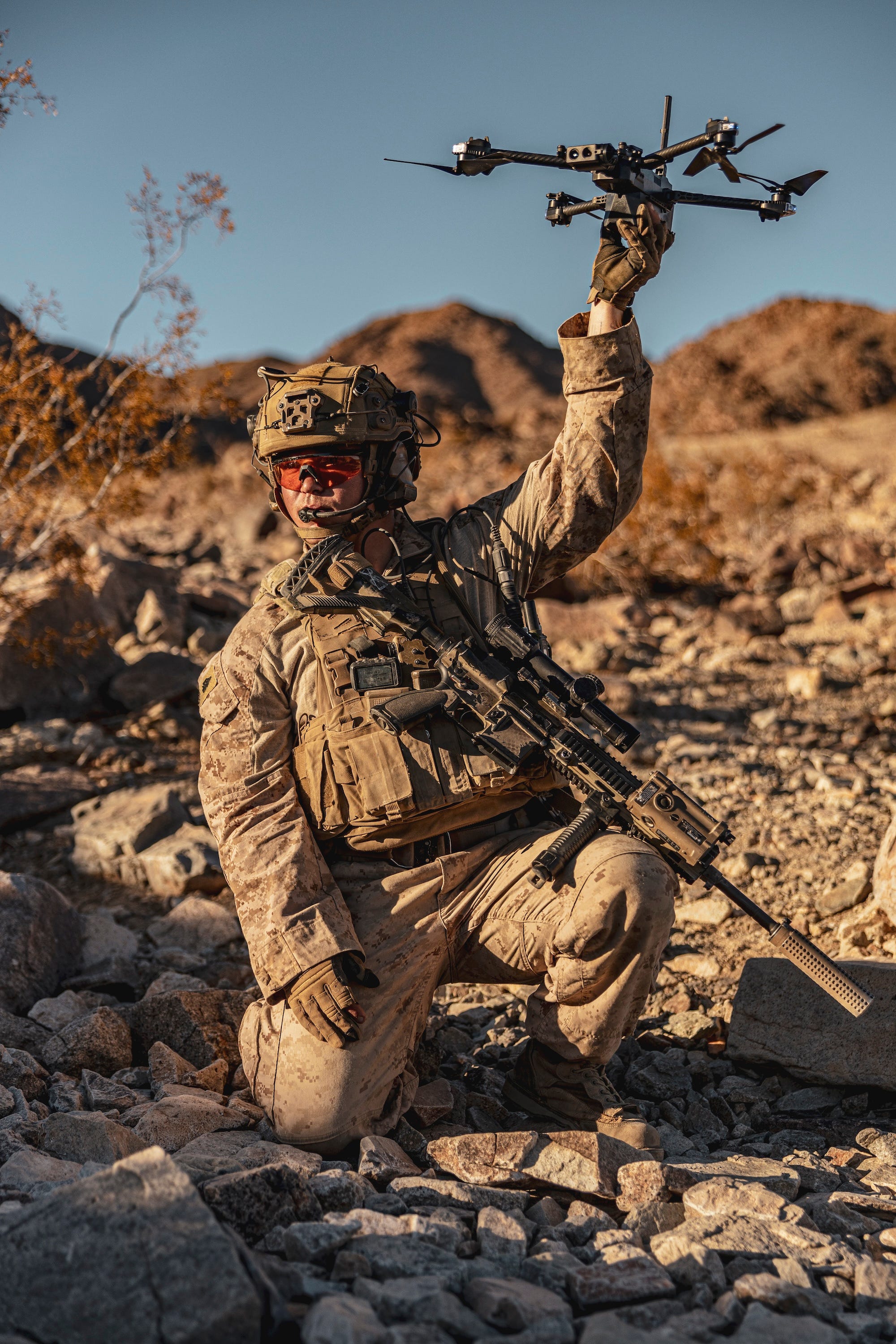A US Marine infantryman holds up a drone in a desert.