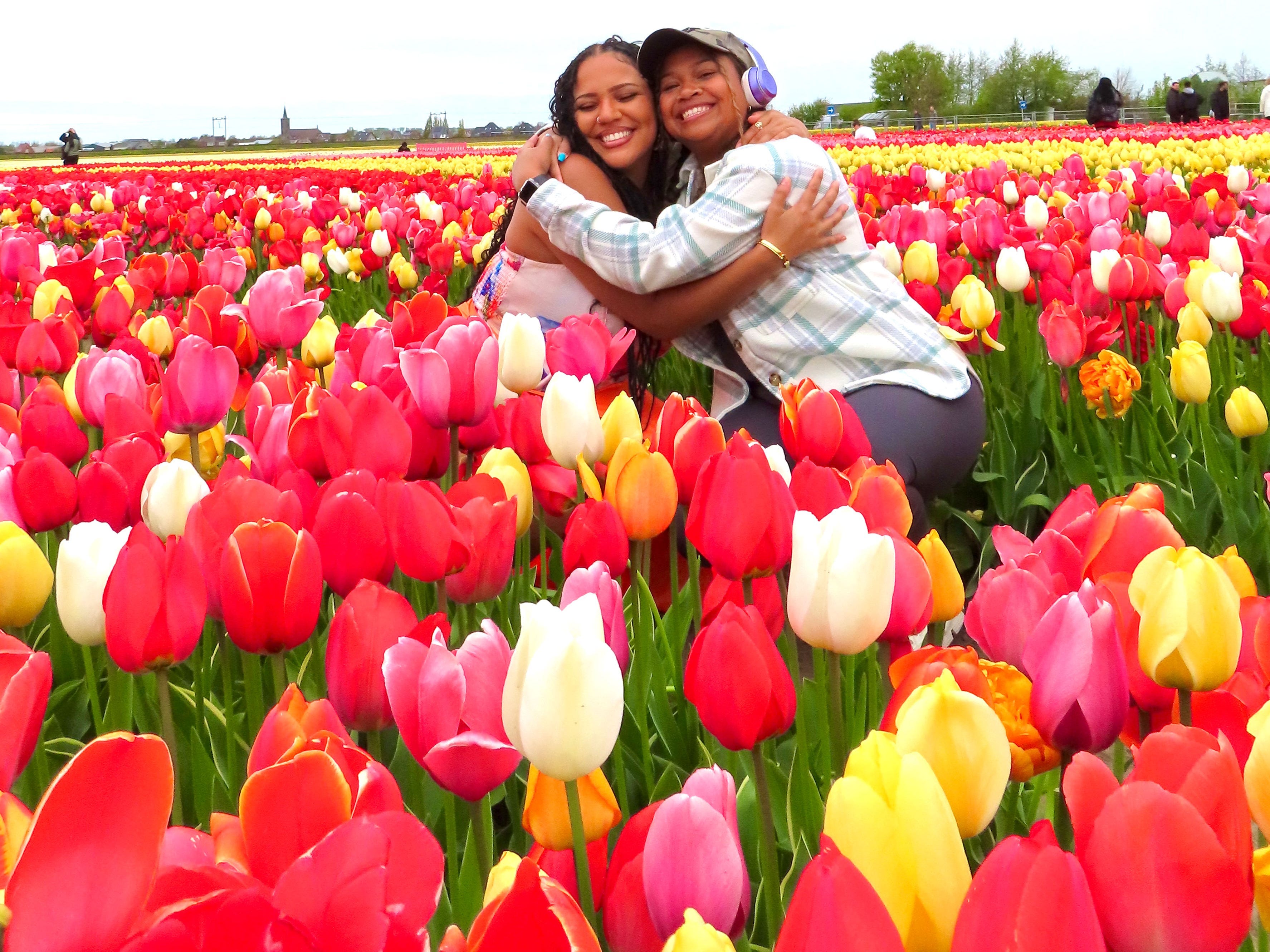 Jasmin and her friend hug while kneeling between rows of colorful tulips.