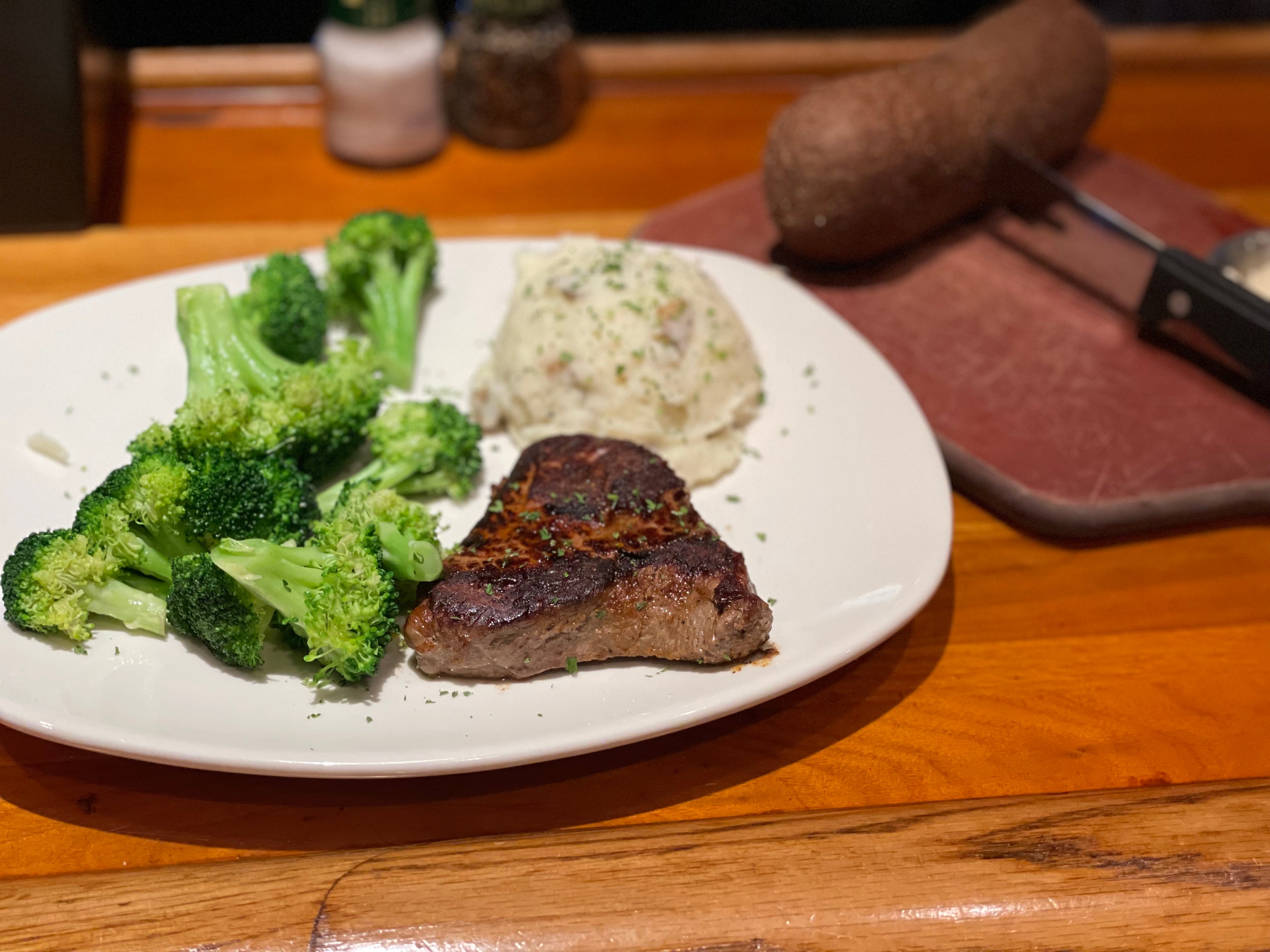 Outback steak, mashed potatoes, and broccoli with loaf of brown bread behind it