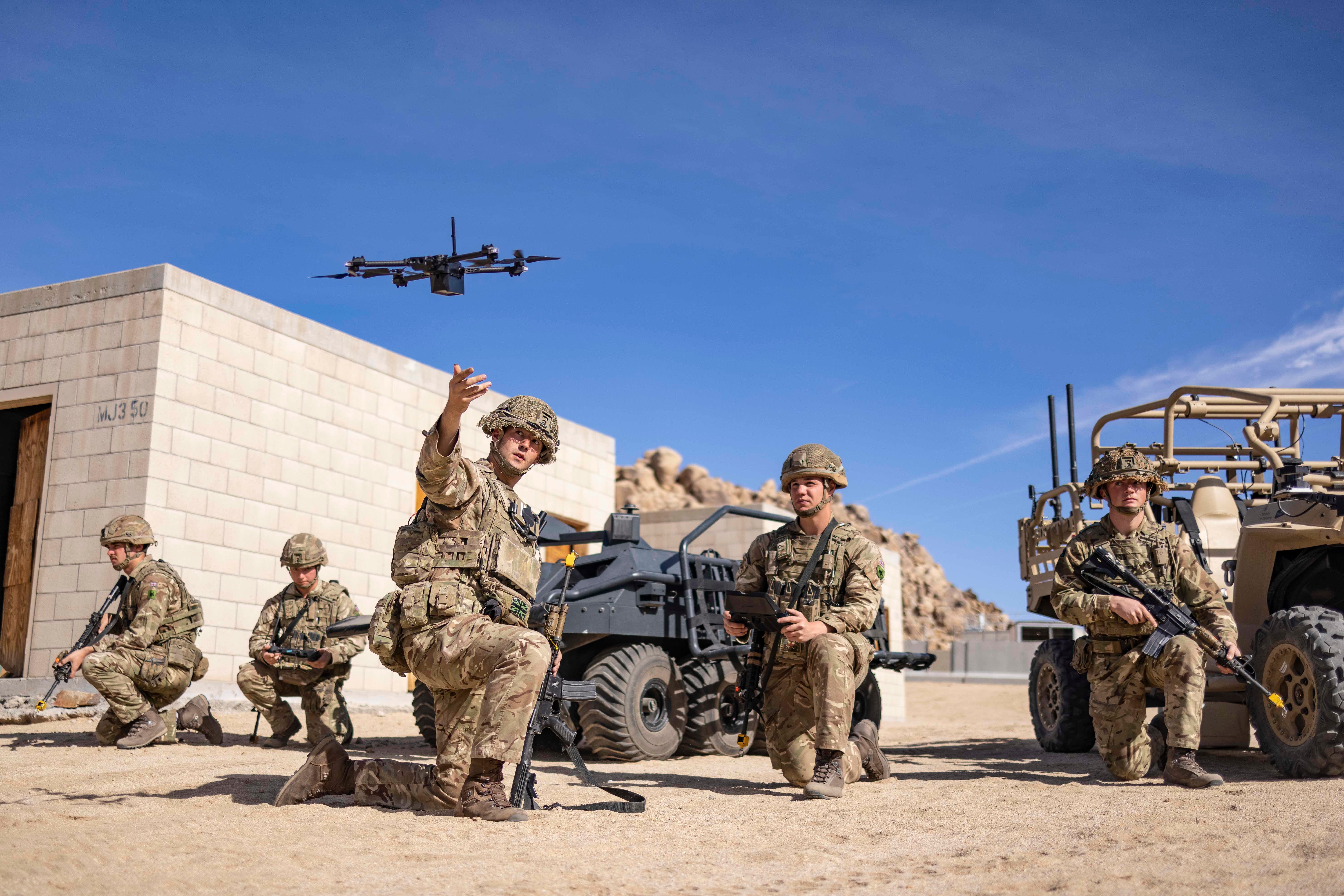 Soldiers operating a quadcopter drone at a training facility on a blue-sky day.