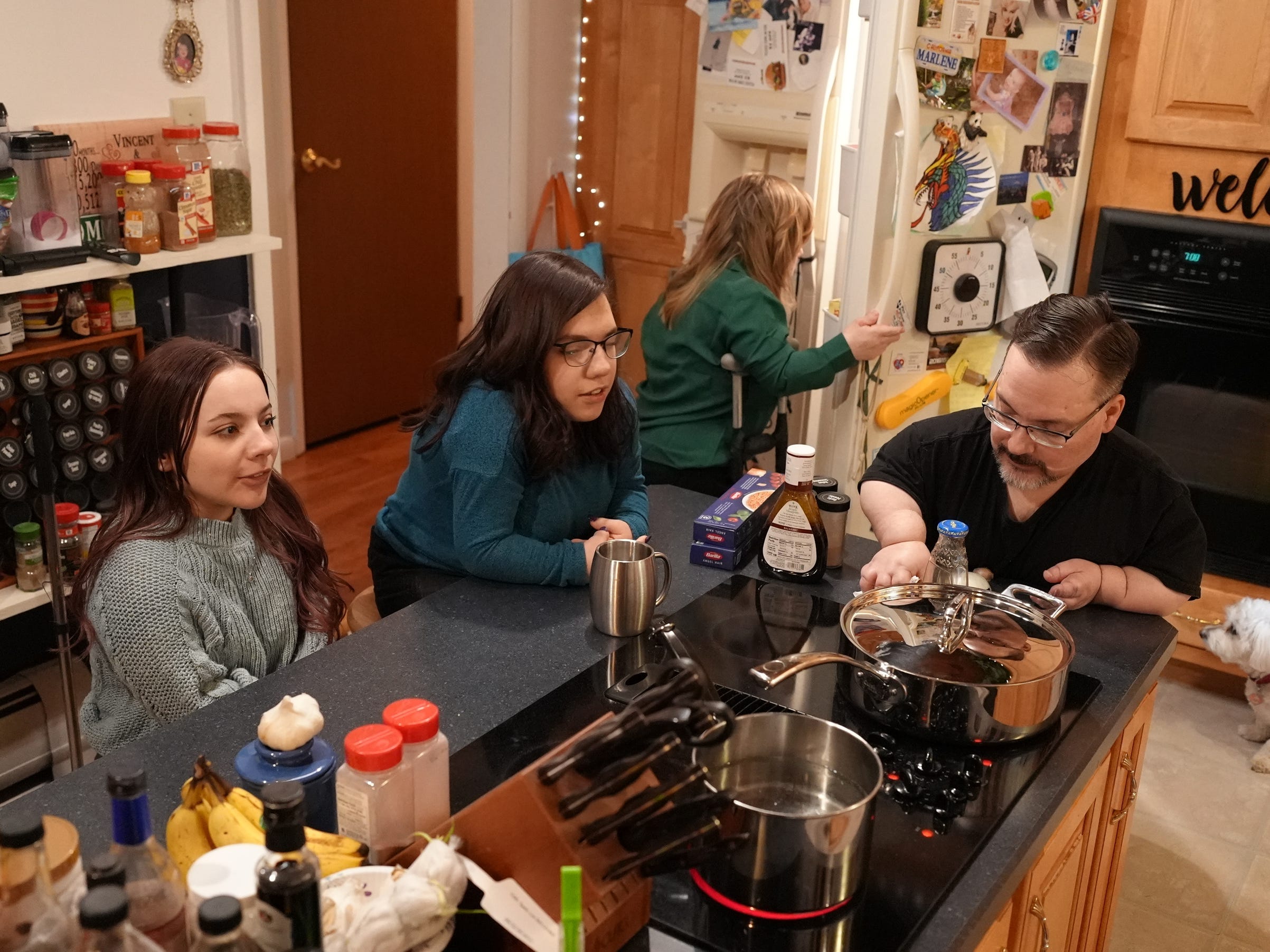 mackenzie depaul, natalia grace, nicole depaul, and vince depaul in the depaul family kitchen. the kitchen is full of cooking ingredients spices, and equipment, and is designed with shorter countertops.