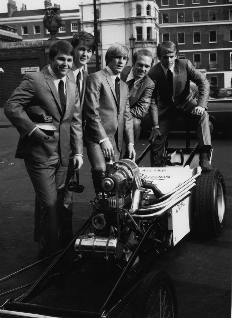 The Beach Boys pose around a dragster in London's West End during a visit to England in 1964 to promote their new single 'When I Grow Up'. From left to right, Carl Wilson (1946 - 1998), Brian Wilson, Dennis Wilson (1944 - 1983) Mike Love and Al Jardine.