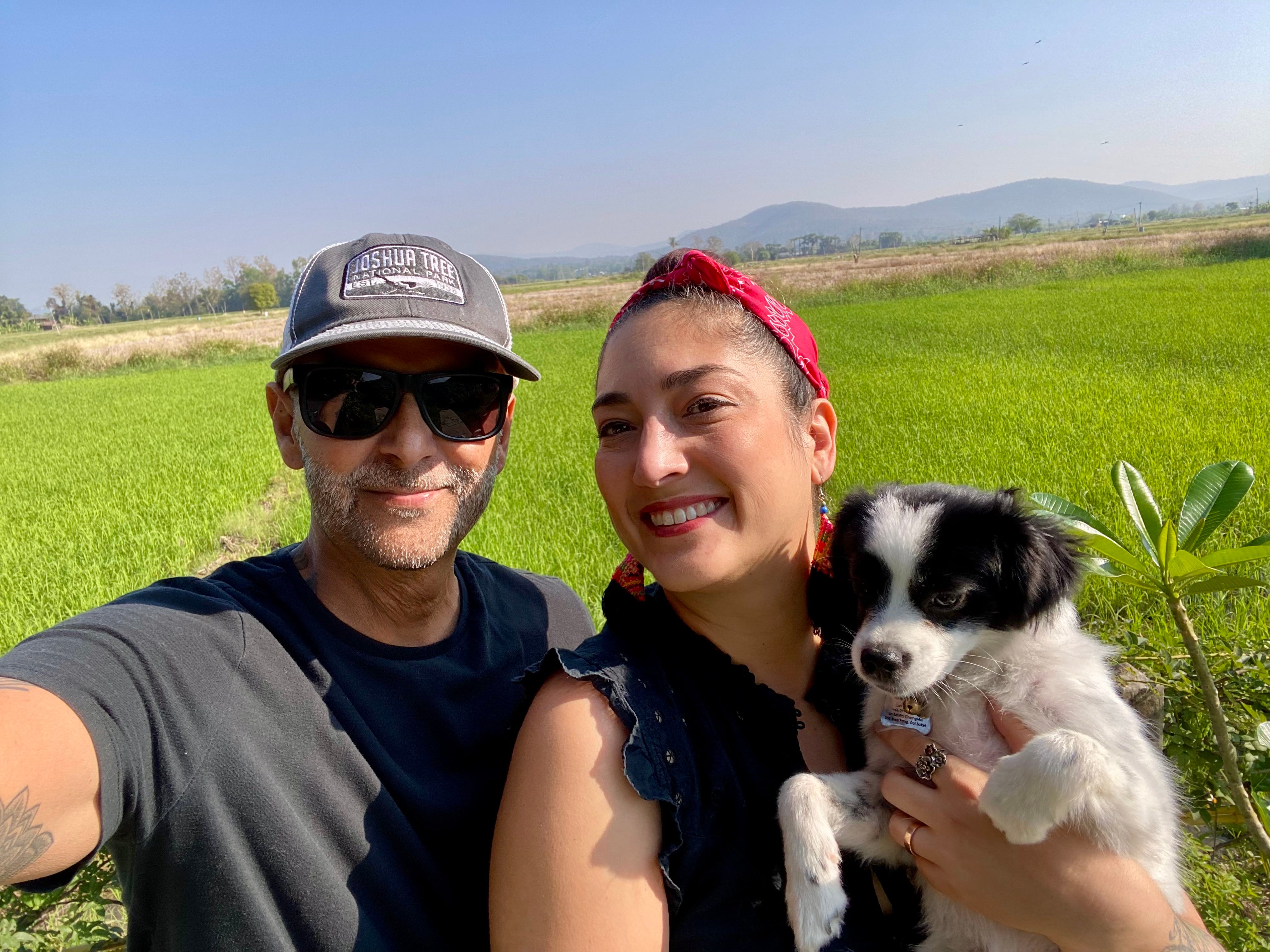 A man and a woman posing with their dog in a field.