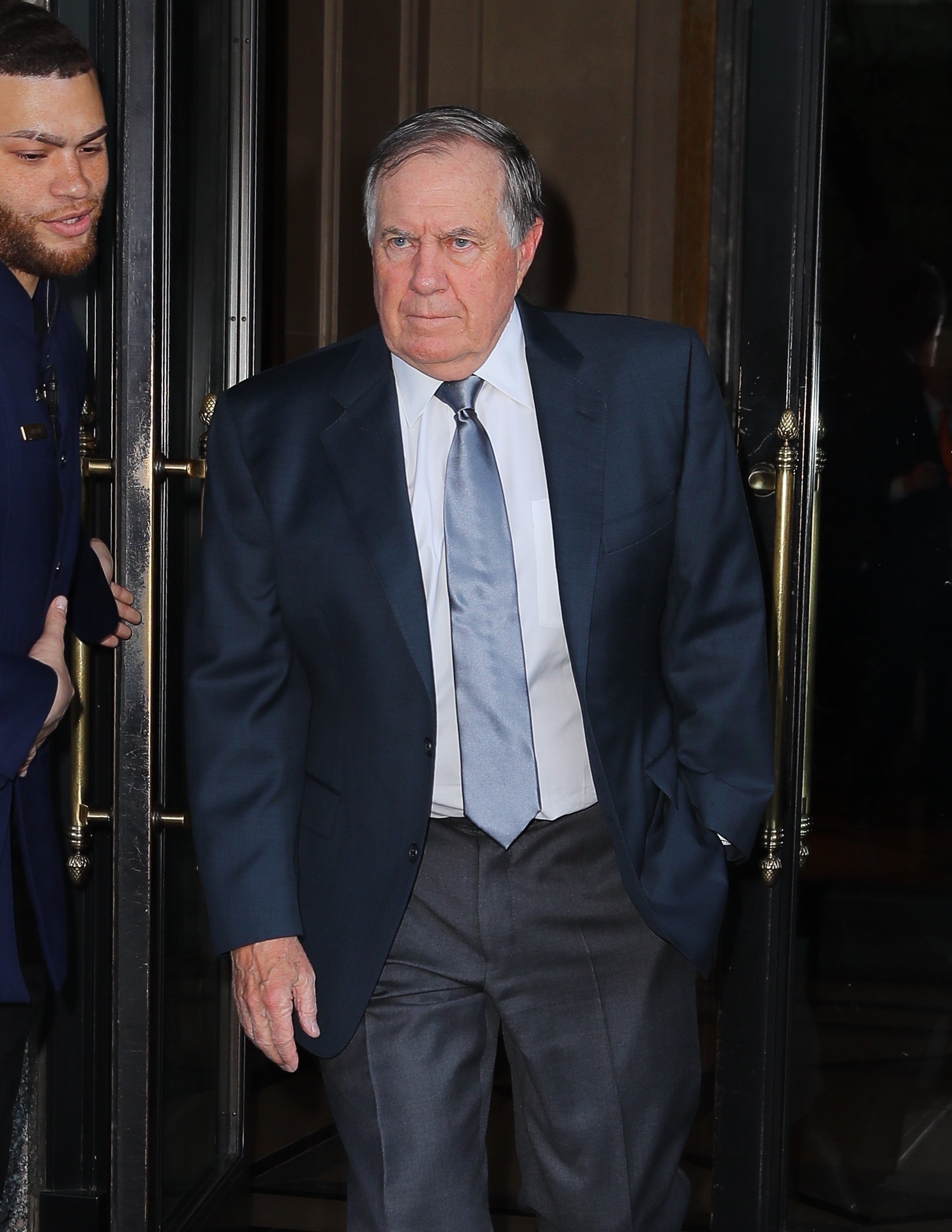 Bill Belichick wears a suit outside a building. 