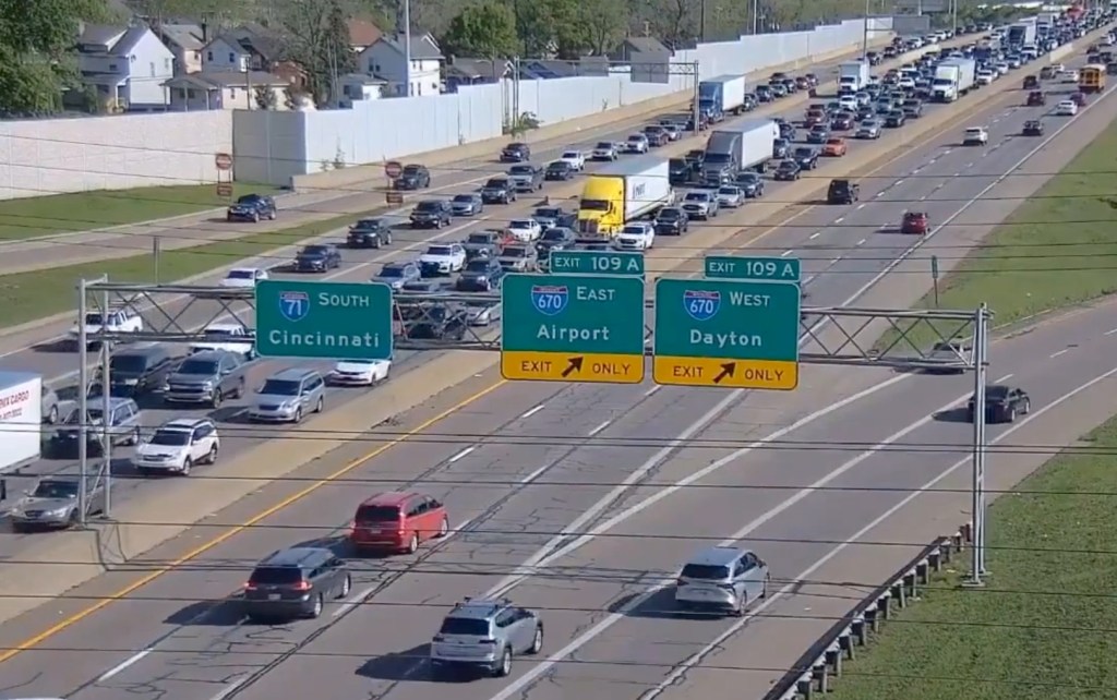 In the clip, a red minivan is seen crawling into the frame in the middle lane of the busy three-lane highway as other vehicles zip around it.