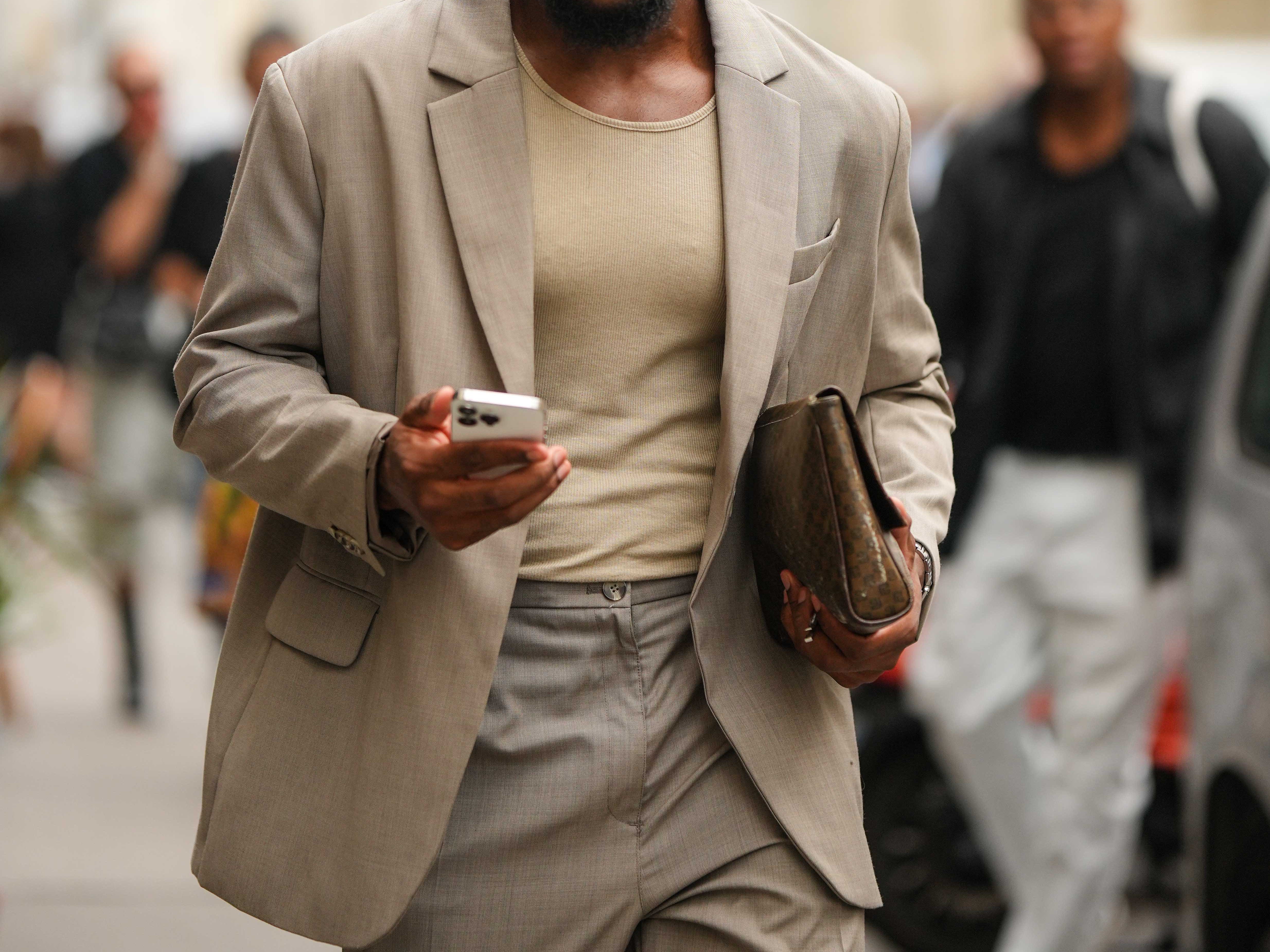 Man wearing blazer and beige shirt below, holdingcheckered bag, wearing sunglasses