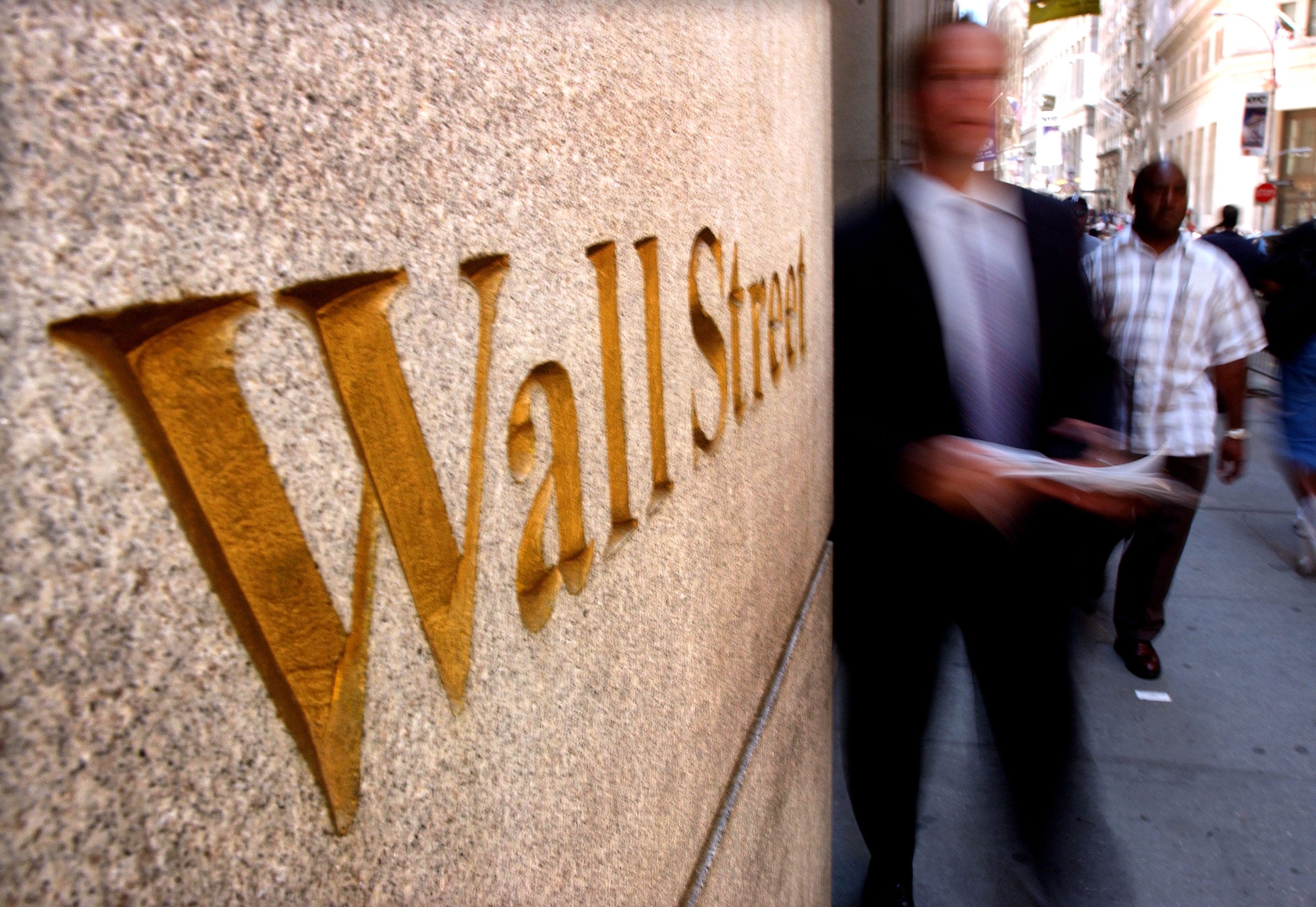 A man in a suit next to a Wall Street sign