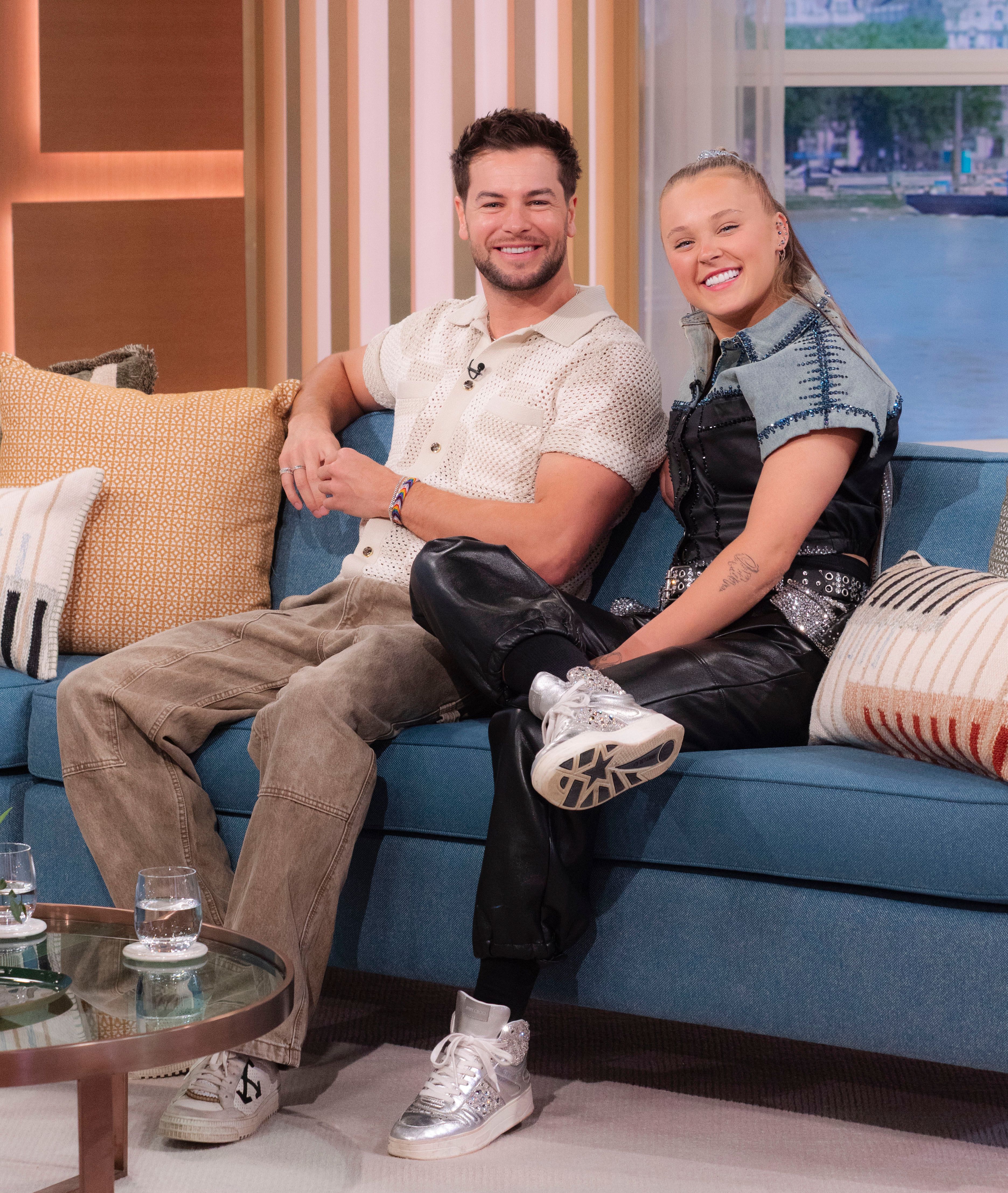 JoJo Siwa and Chris Hughes laughing on a couch. 