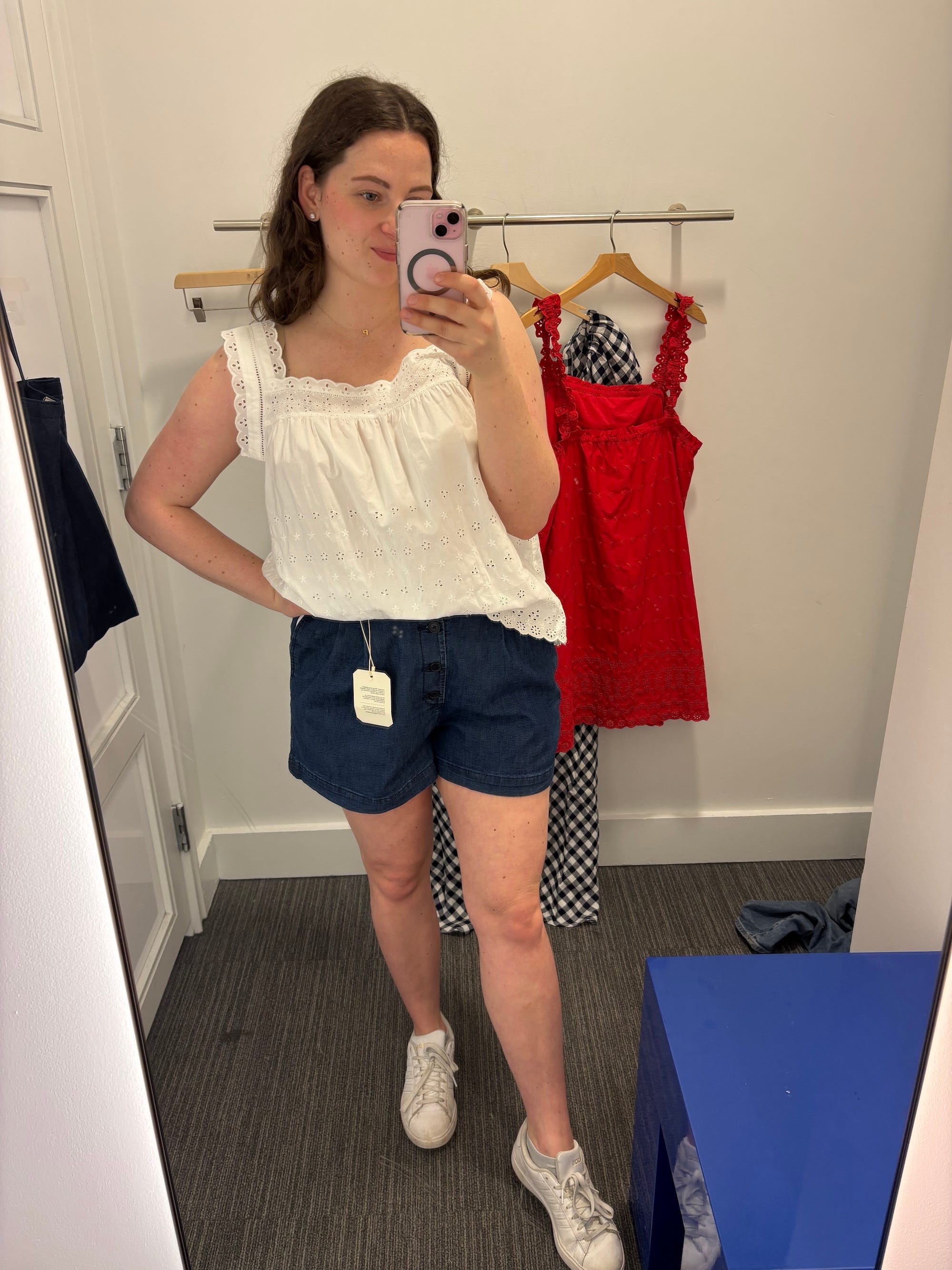 A mirror selfie of a woman in a white shirt and denim shorts.