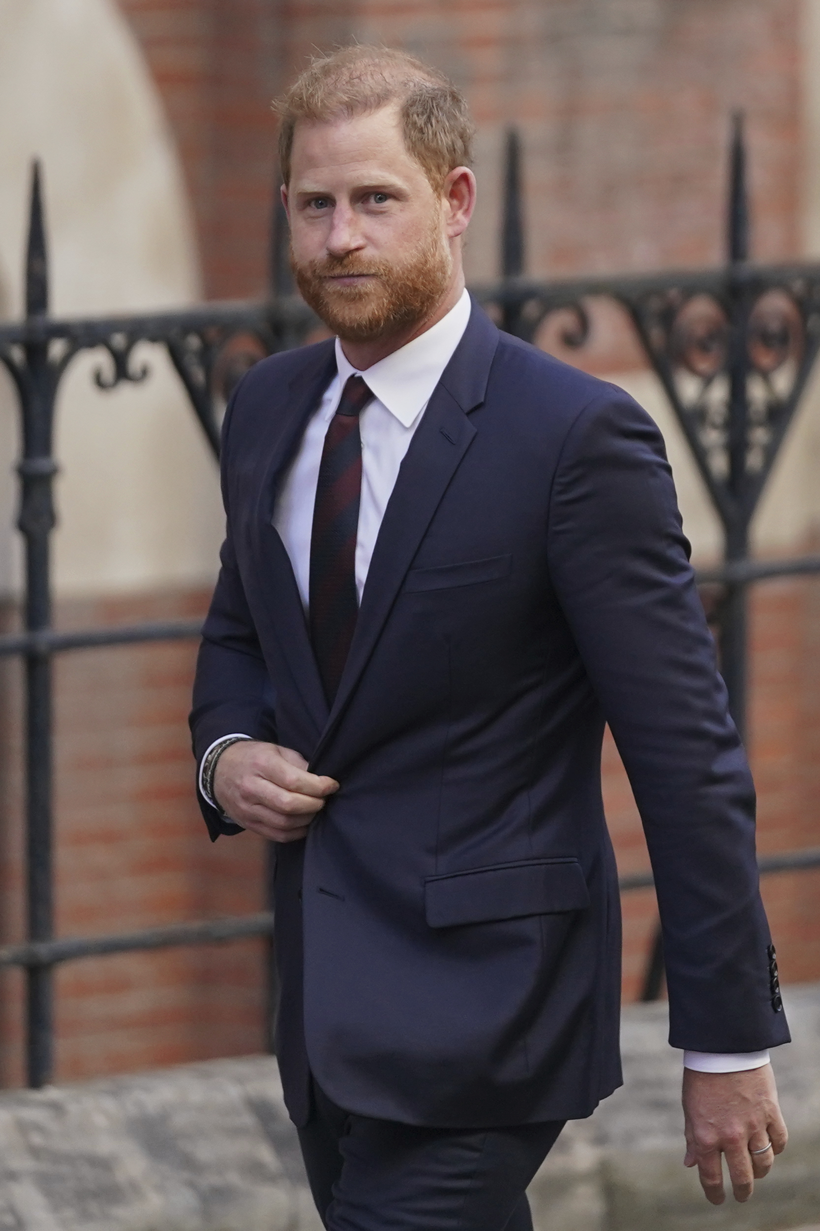 Prince Harry walks outdoors in a suit. 