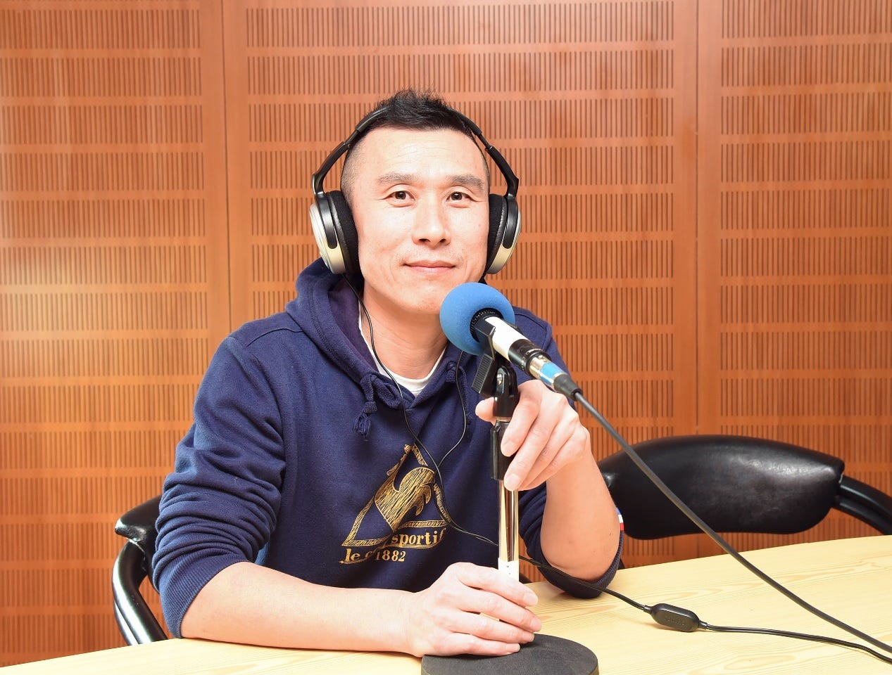 Li Yanhe in blue sweatshirt in front of microphone with headphones on