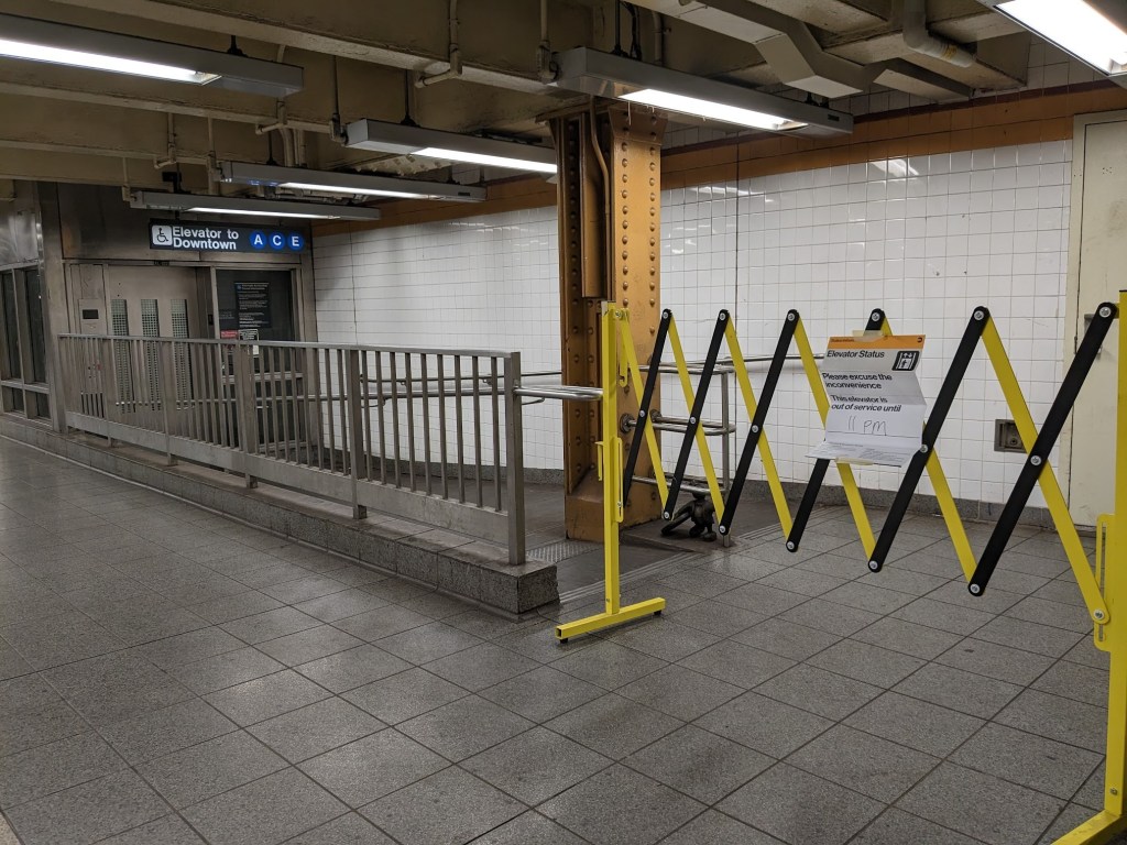 A yellow barrier blocking access to a ramp and the elevator that says elevator out of service