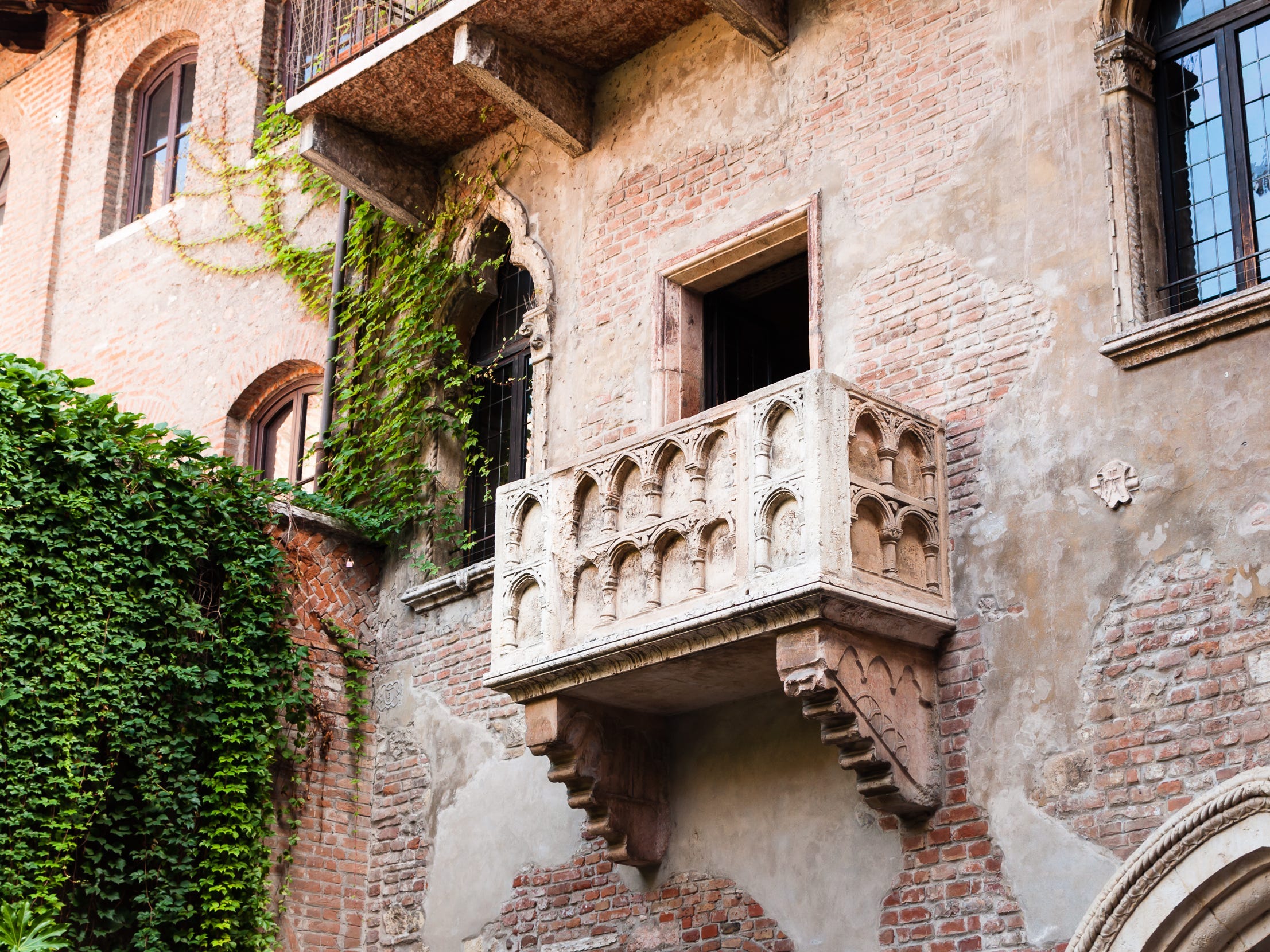 A stone balcony on a brick building that's partially covered in ivy.
