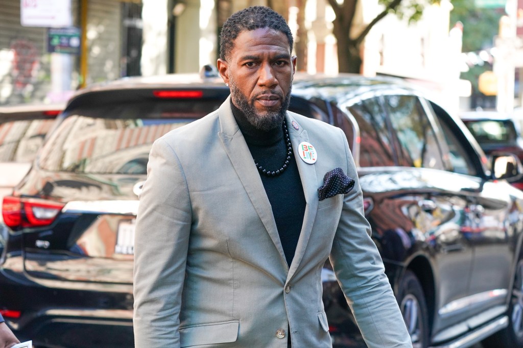 jumaane williams in a grey suit and black shirt with black and white pocket square outside on the street.