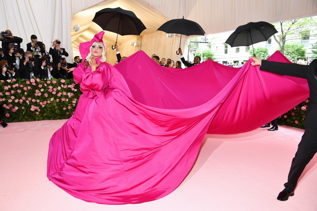 Lady Gaga in massive pink dress with black umbrellas being held up in the background. 