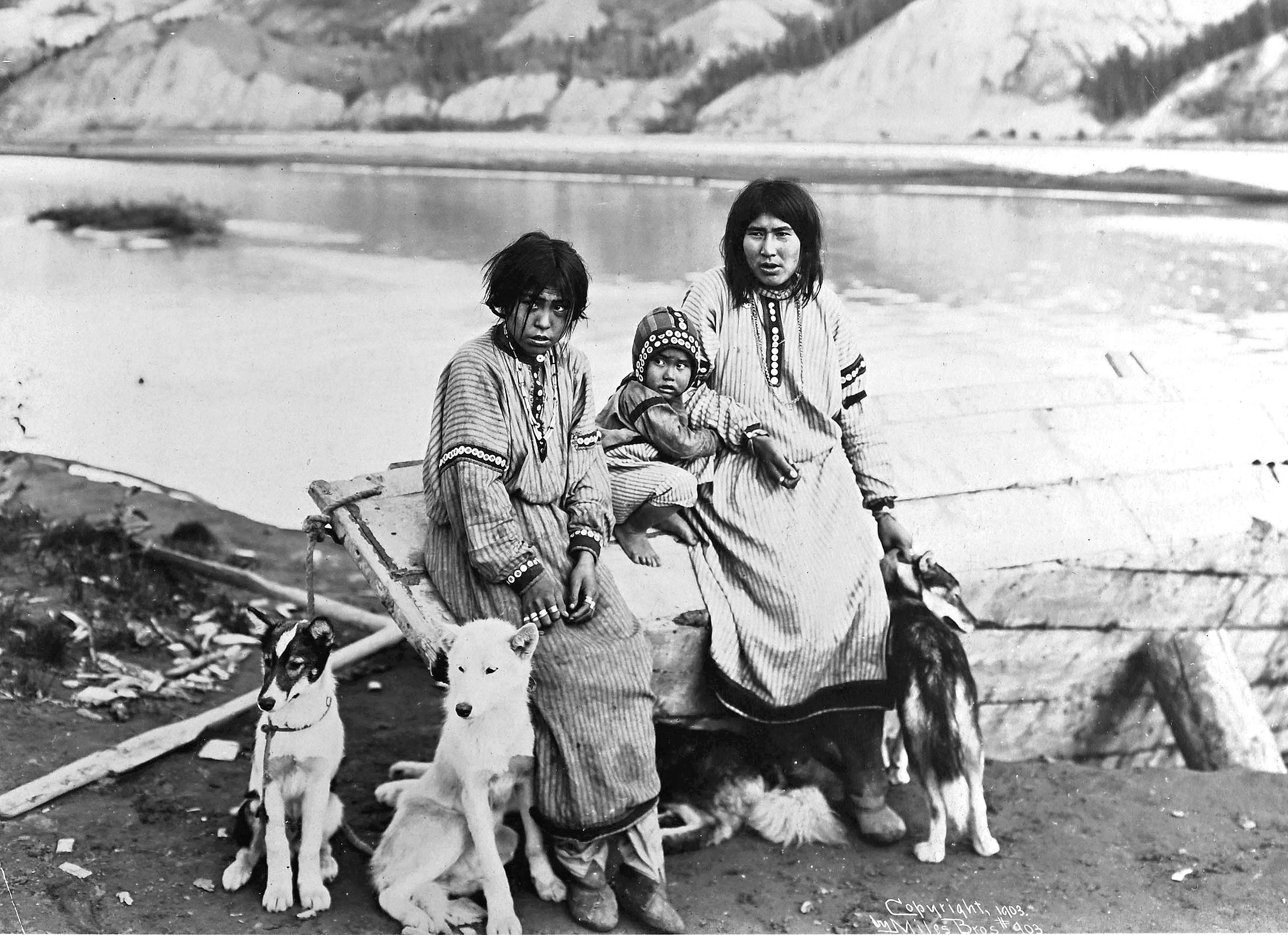 Three members of a family sit with their dogs beside a river.