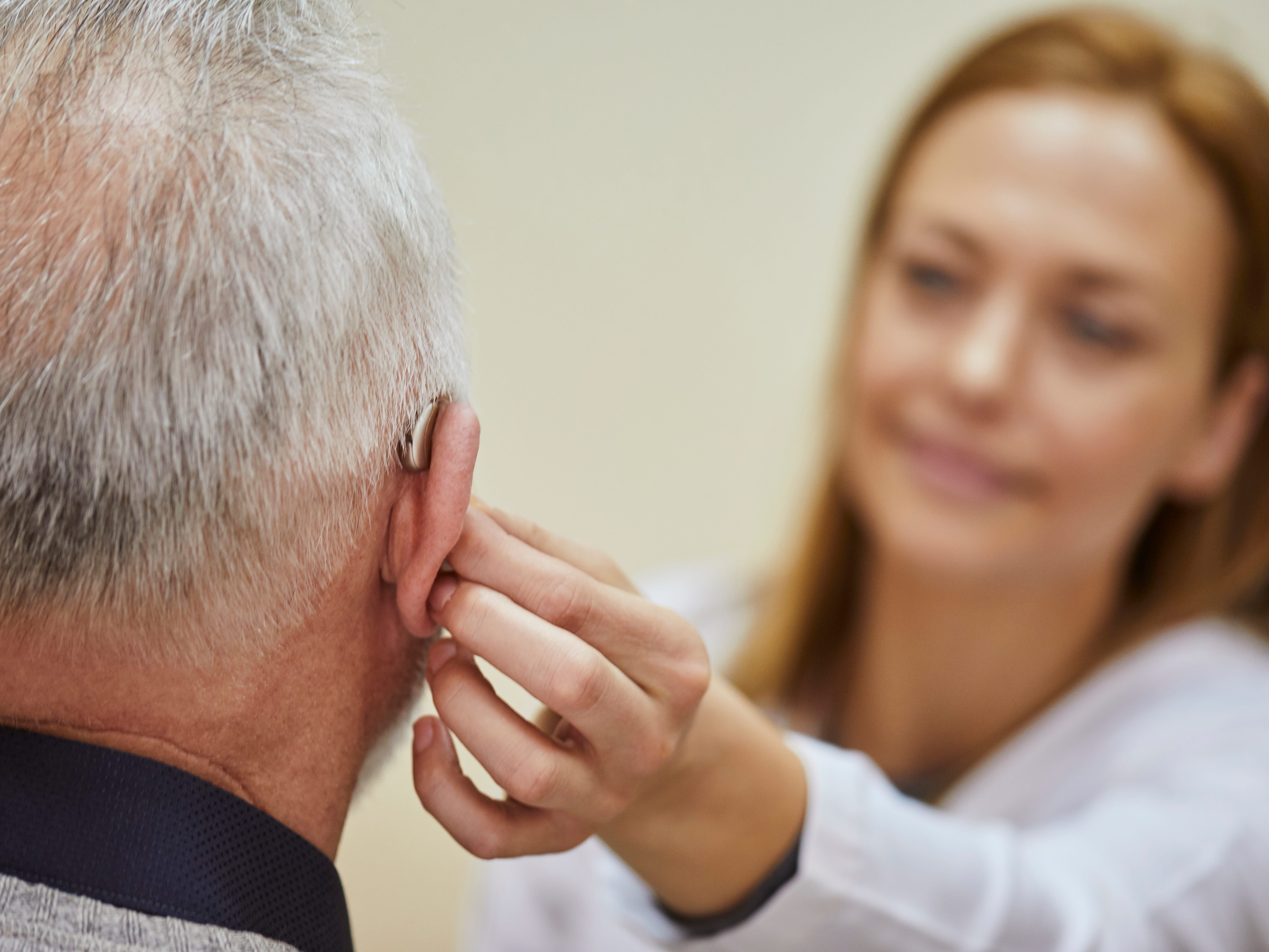 A healthcare worker or doctor helping a patient with a hearing aid