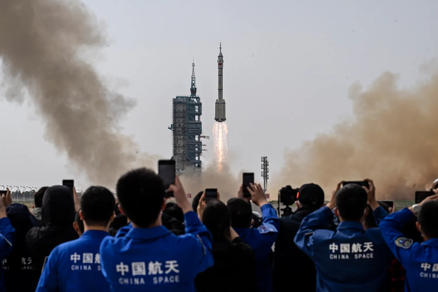A crowd of people with their phones up watch a rocket launch.