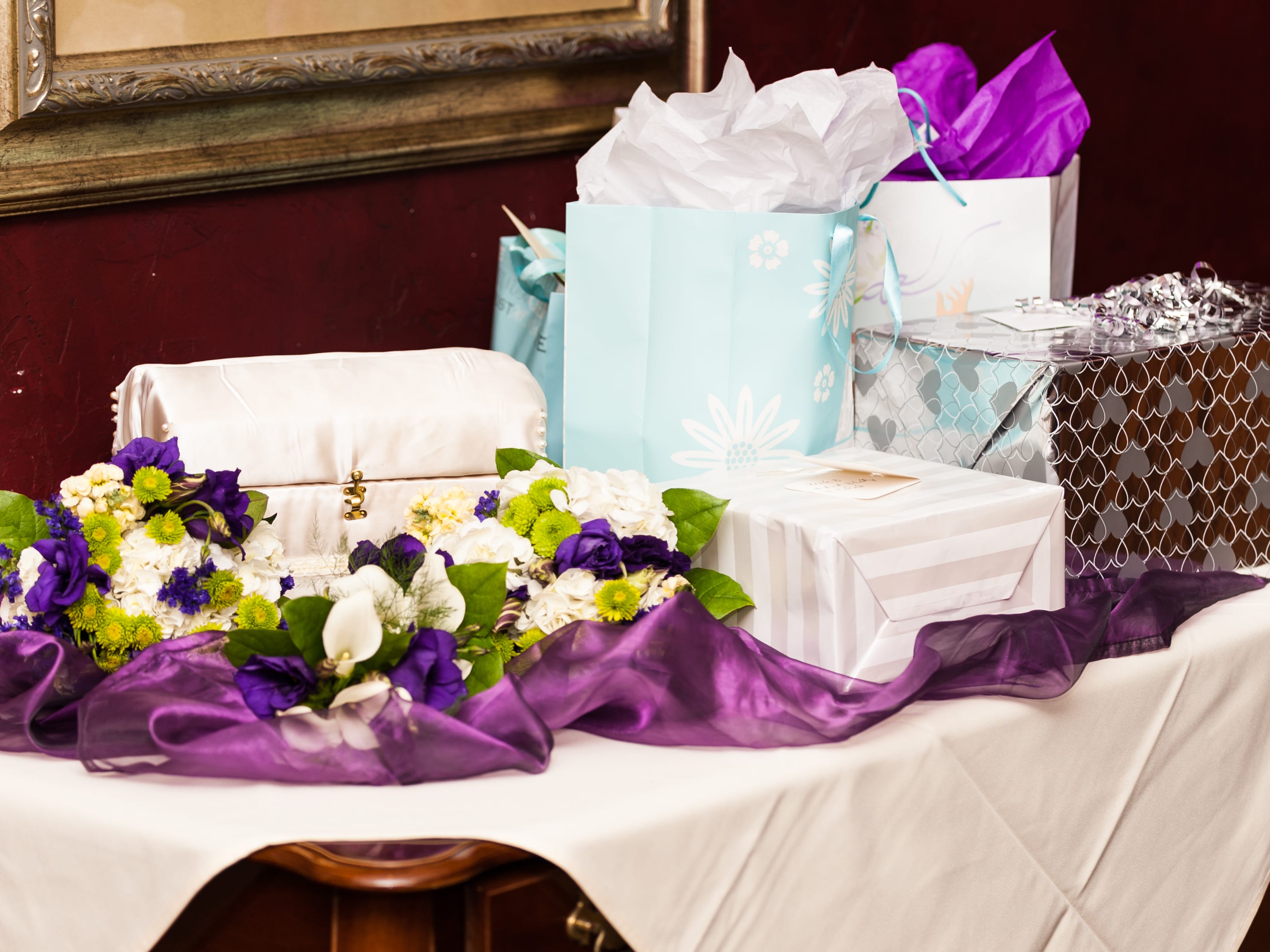 A table of gifts with purple ribbon, flowers, and a white cardbox.