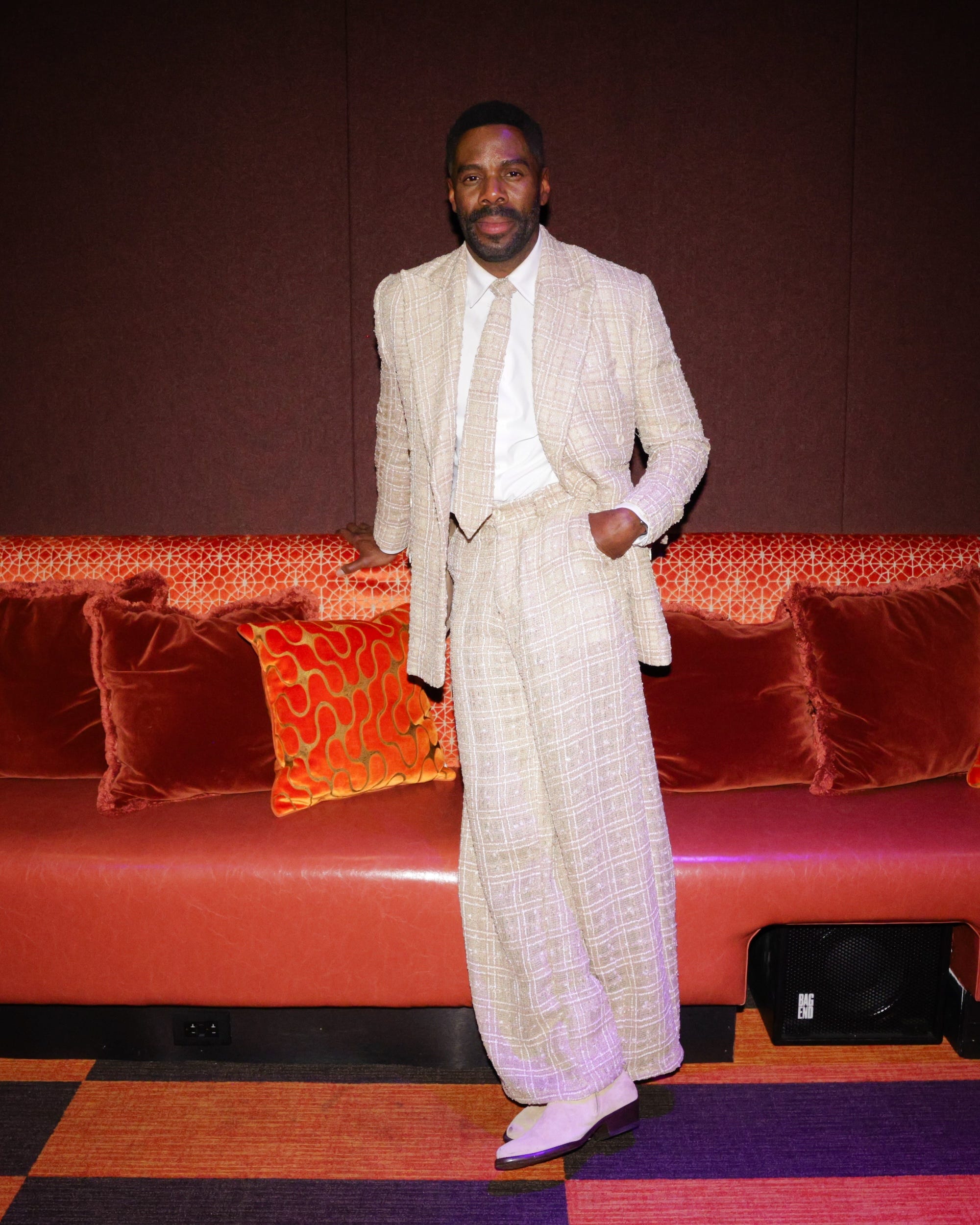 Colman Domingo in a textured suit in front of a red couch.