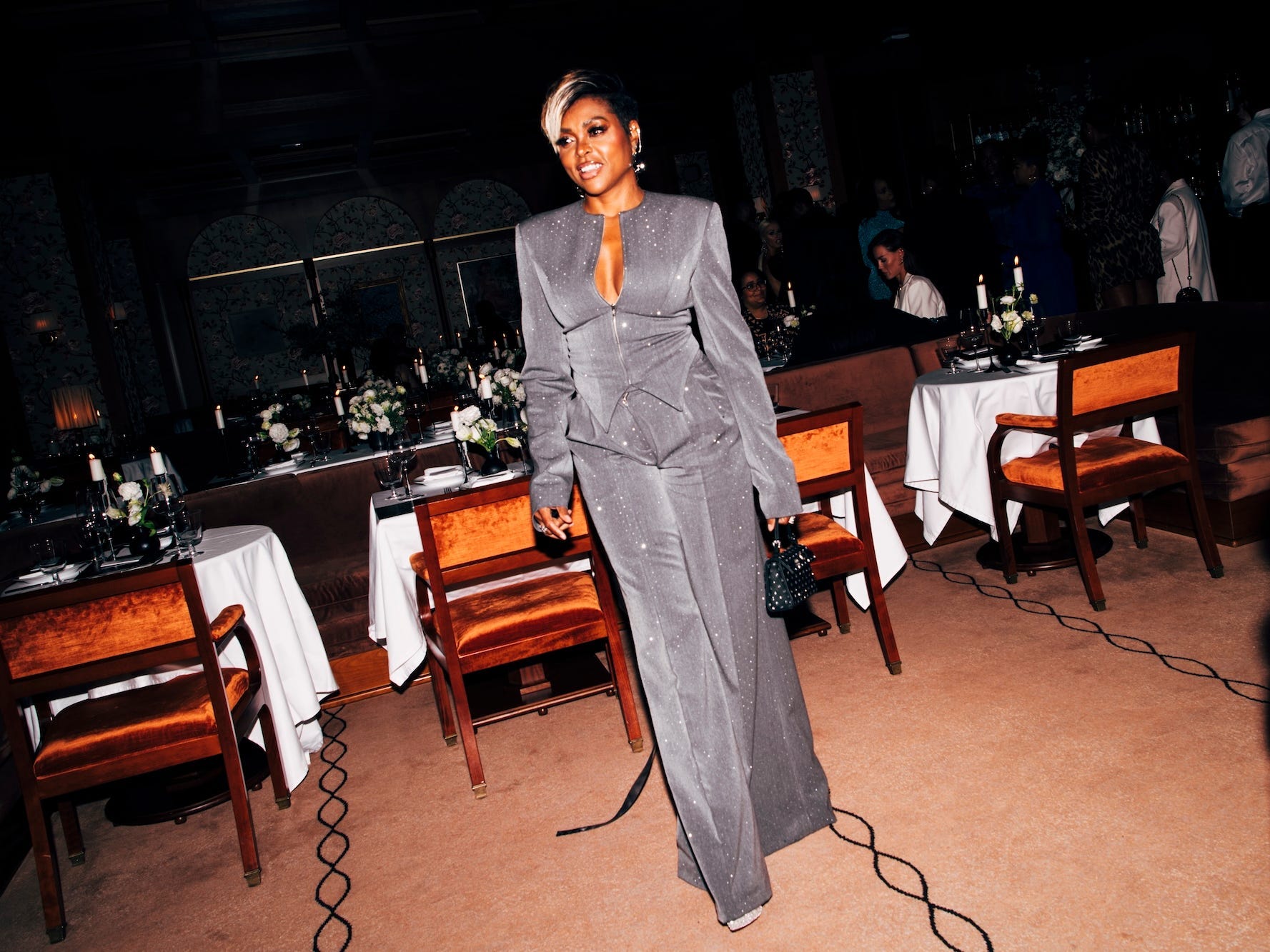 Taraji P. Henson stands in a gray, sparkly suit in a restaurant.