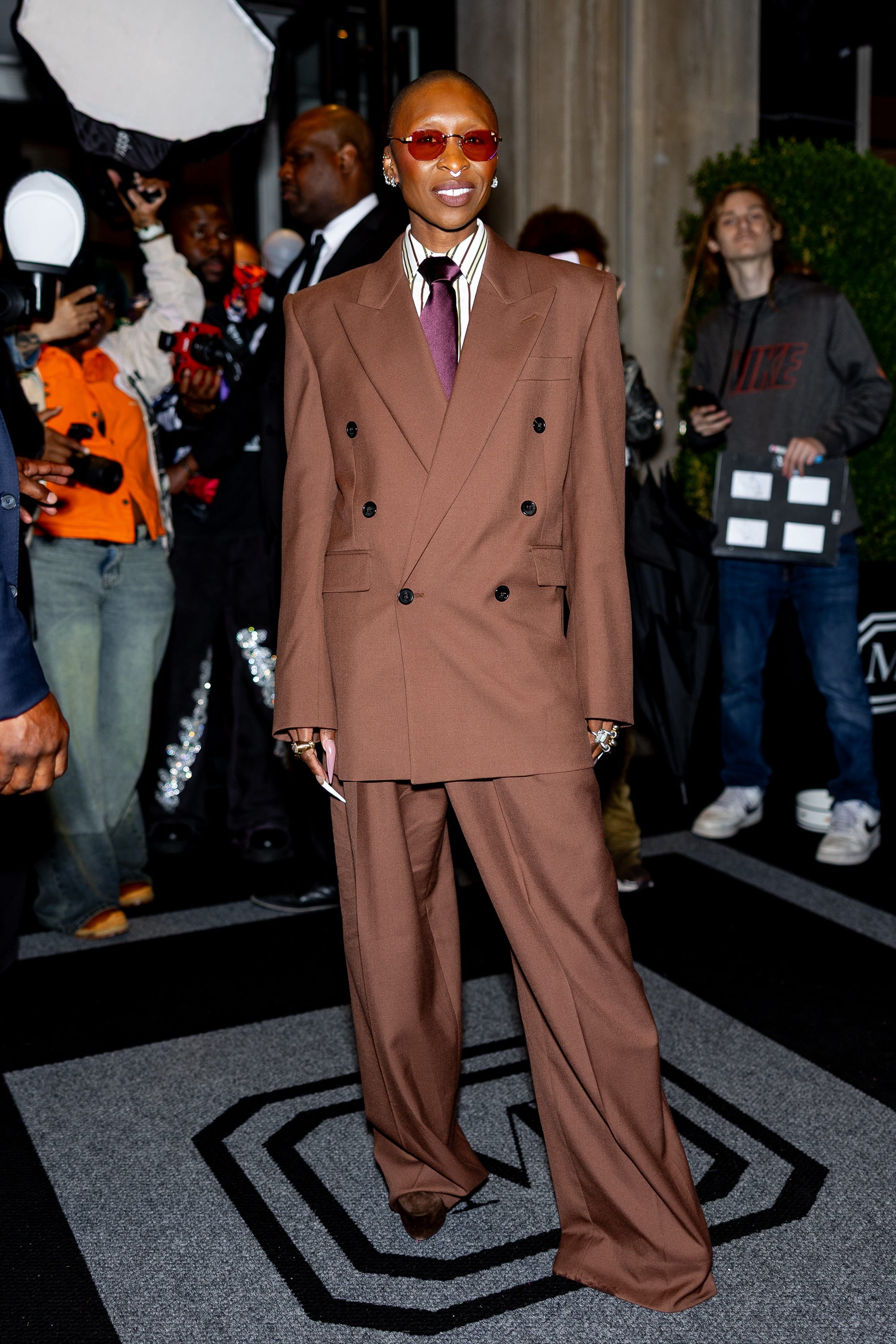 Cynthia Erivo stands in a brown suit and sunglasses.