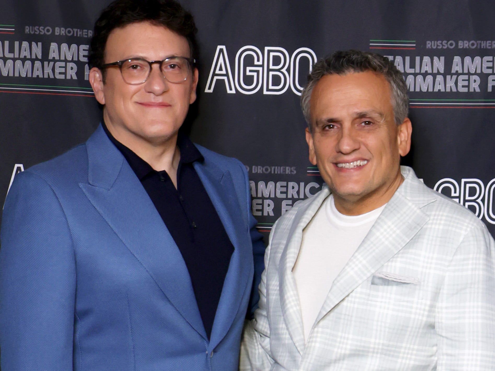 A picture of Anthony Russo in a blue suit and Joe Russo in a white suit at a black carpet event.
