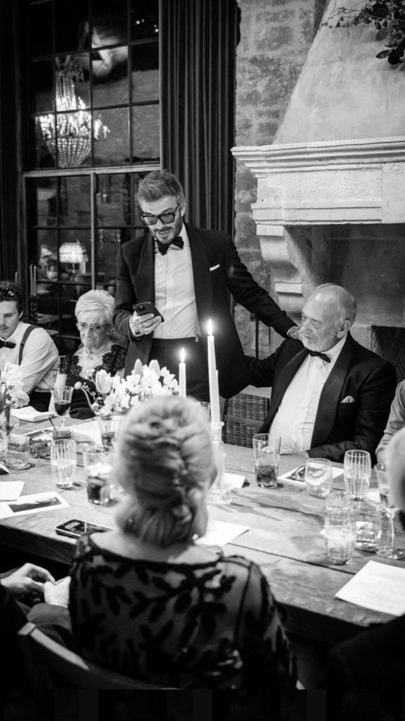 David Beckham standing next to his father, also named David, who is seated at a table with many others