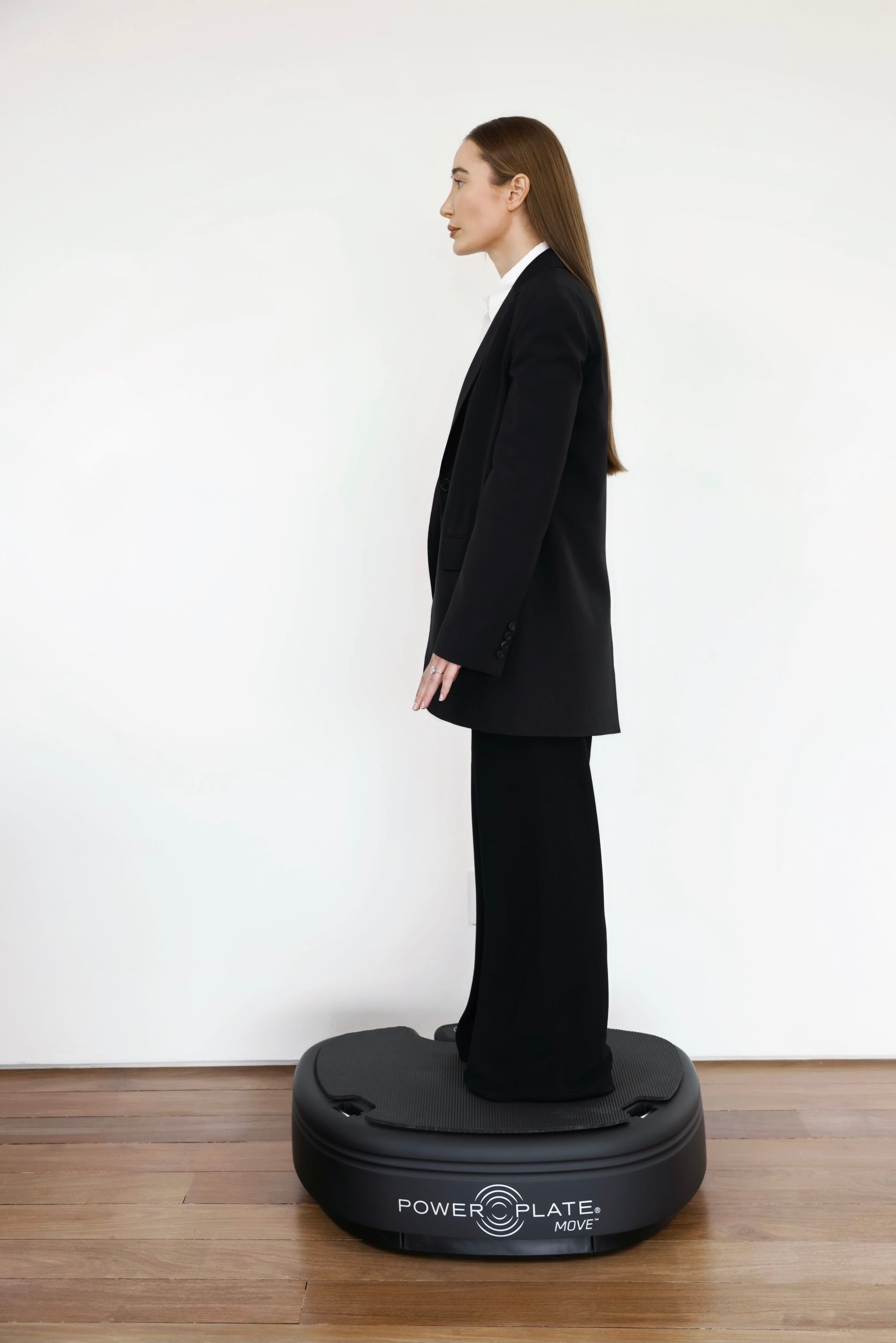 A woman in a suit, standing on a vibration plate.