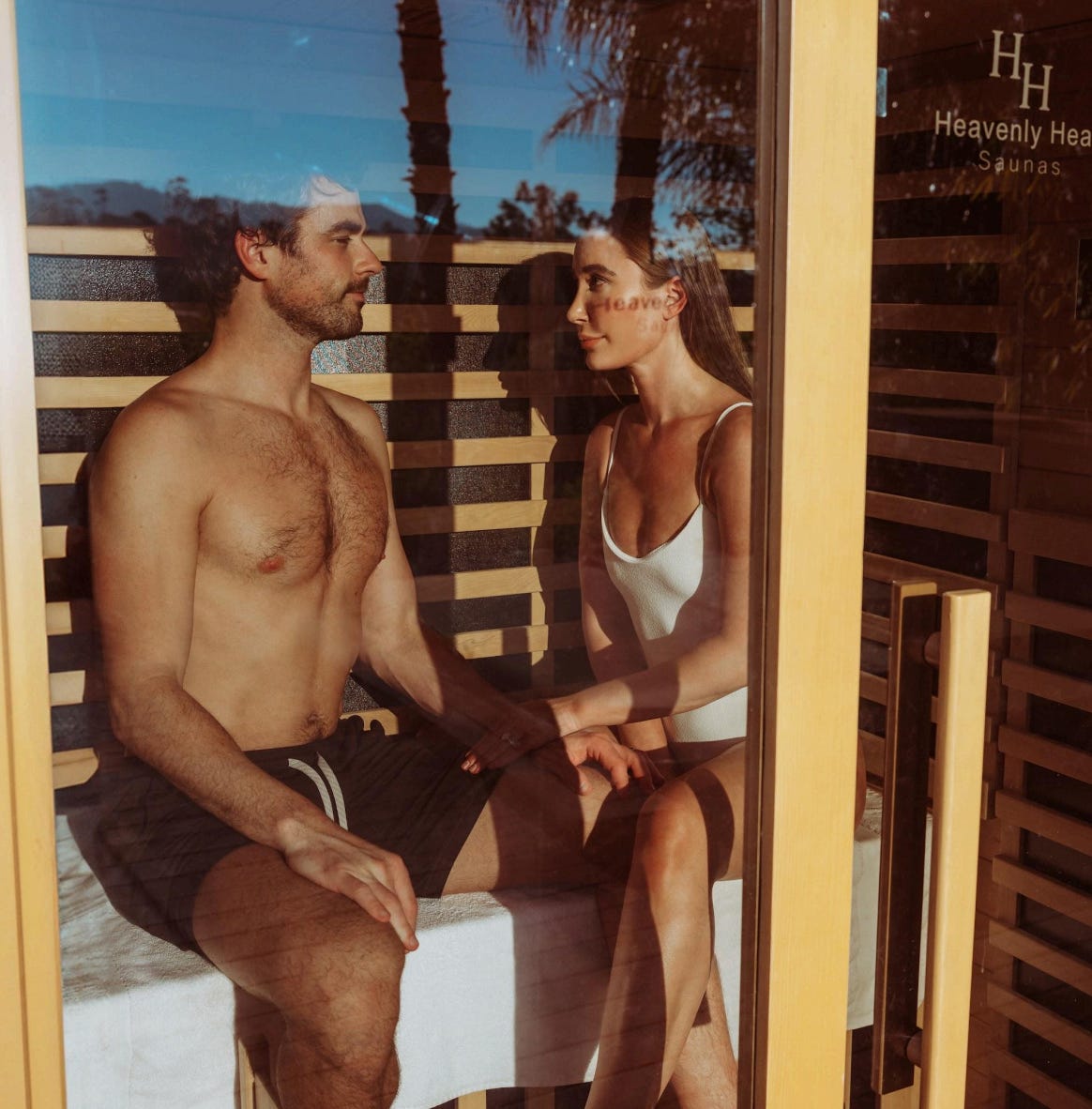 A man and a woman in a sauna, holding hands.