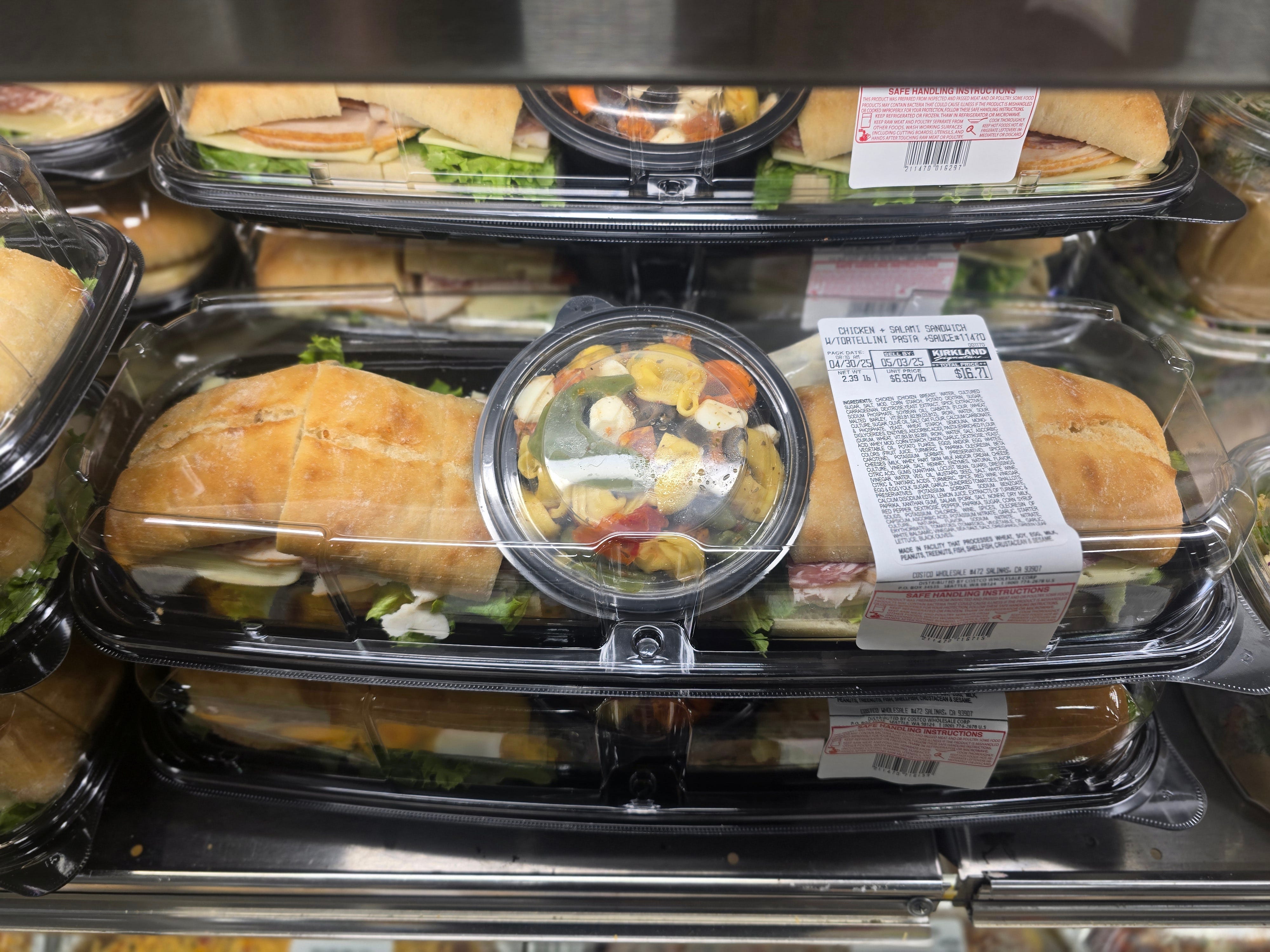 Two sandwiches and a container of tortellini salad in a larger container.