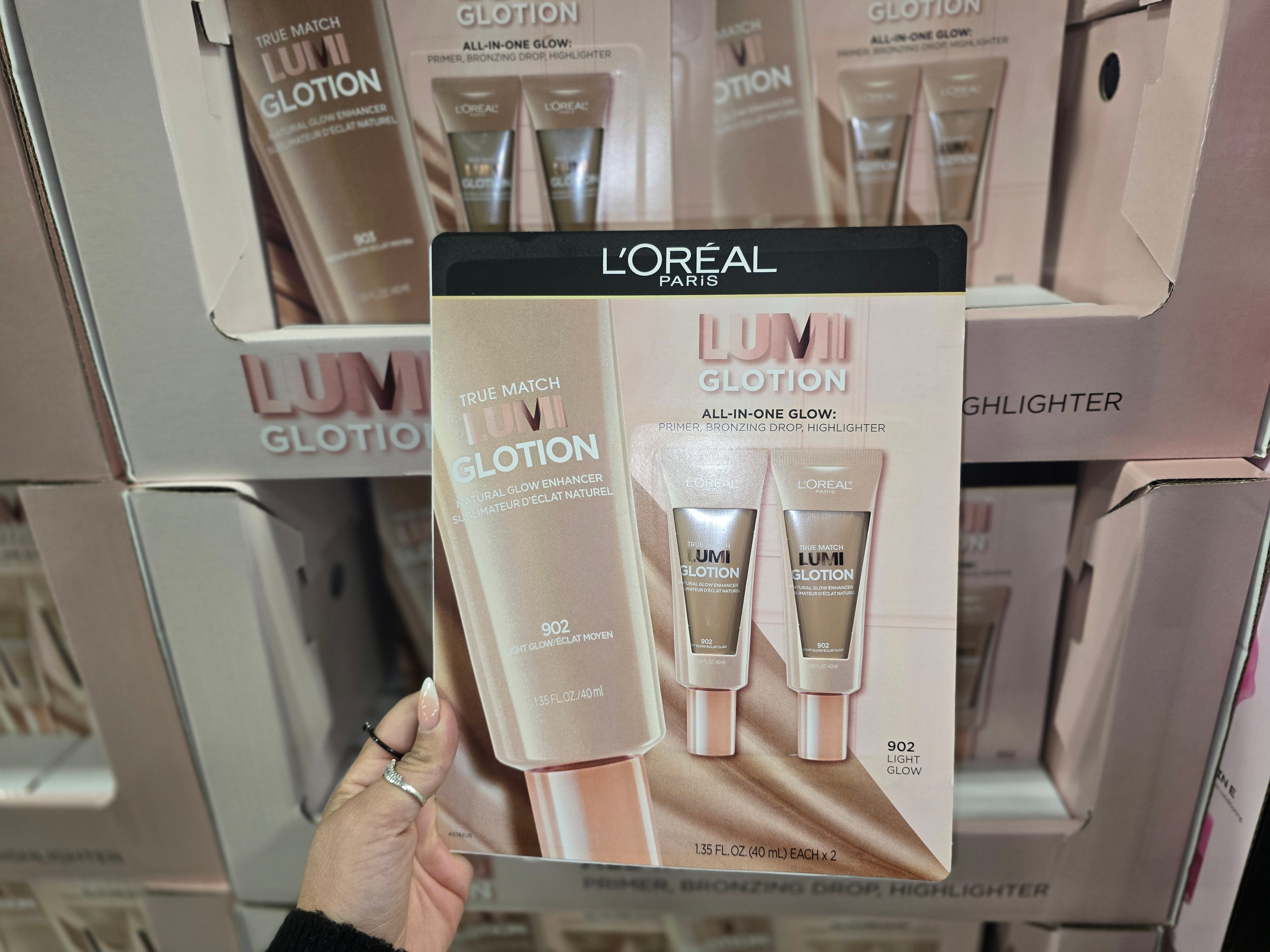 A woman's hand holding a twin pack of L'Oreal Paris Lumi glow lotion.