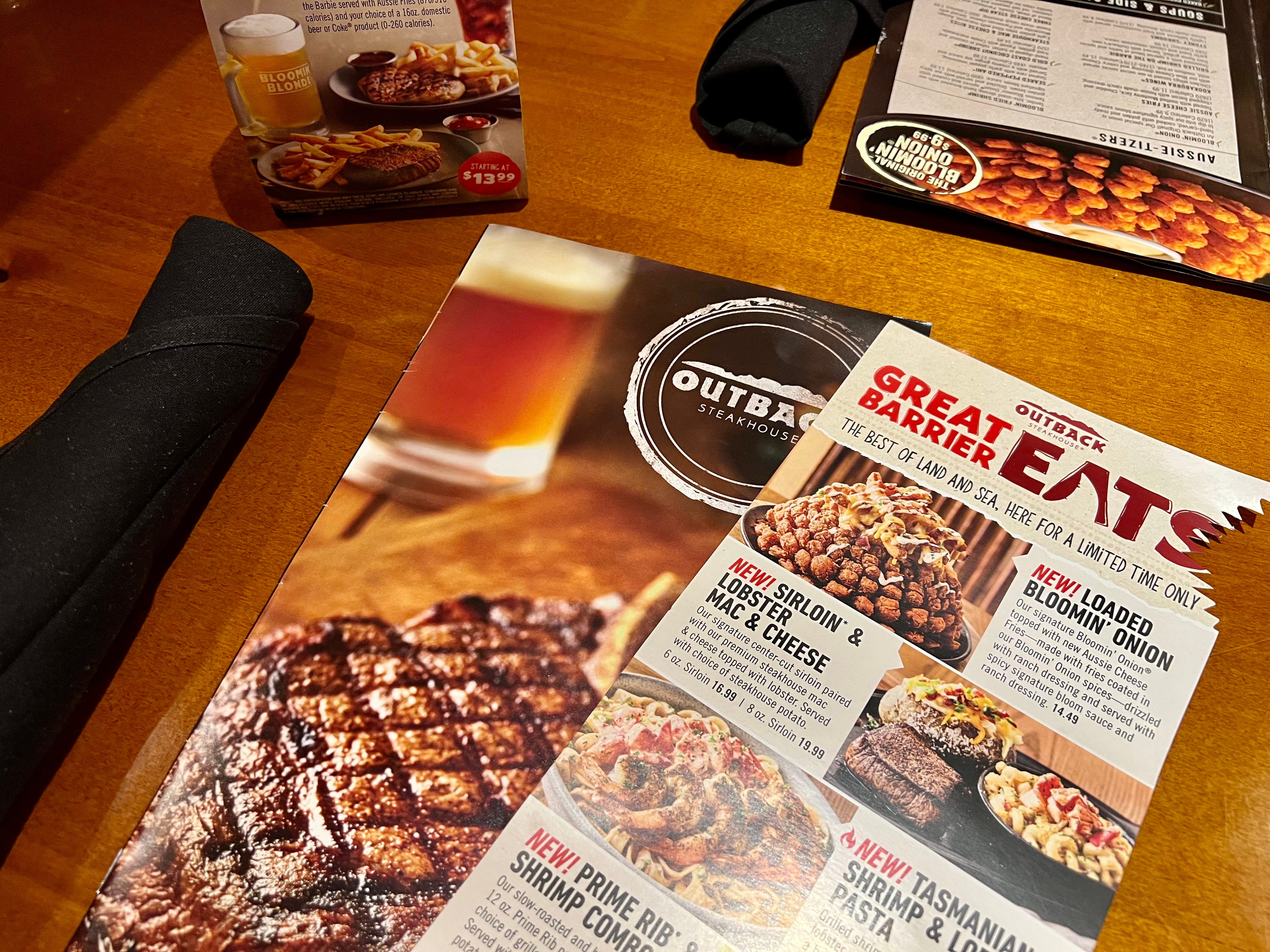 Outback Steakhouse menus and napkins on a wooden table.