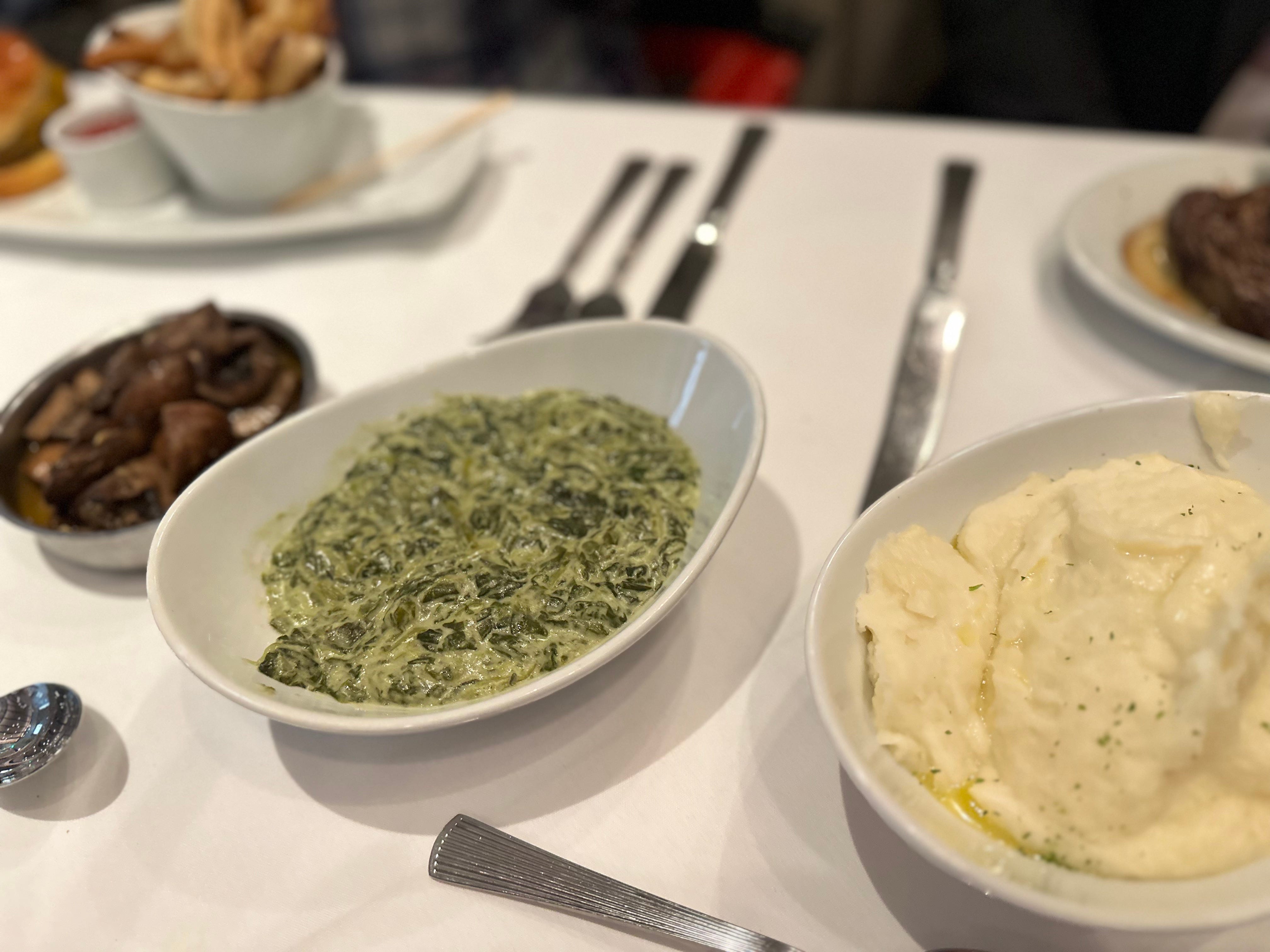 Bowls of mushrooms, creamed spinach, and mashed potatoes on a white table cloth.