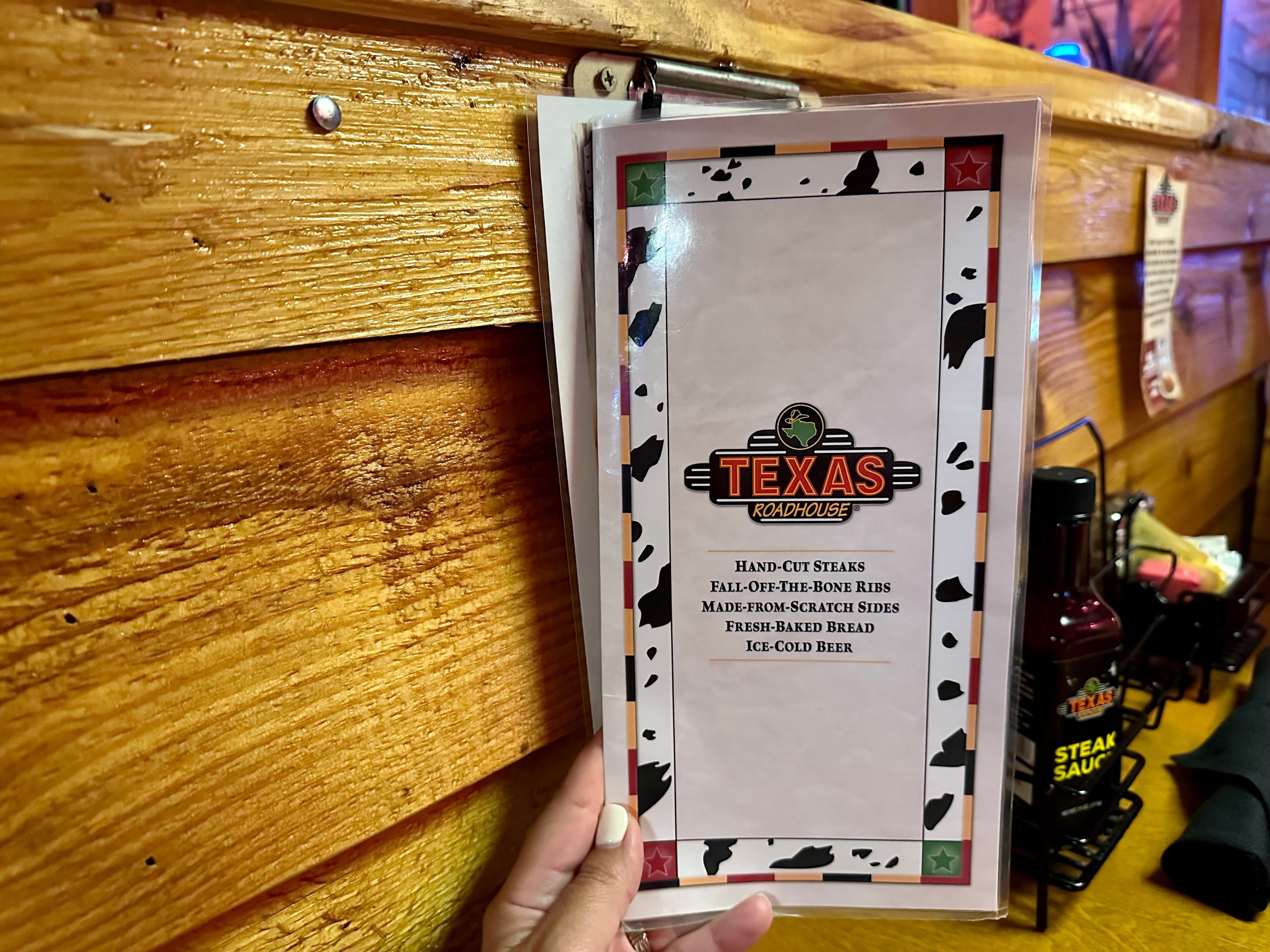 Hand holding Texas Roadhouse menu in front of wood paneling in restaurant
